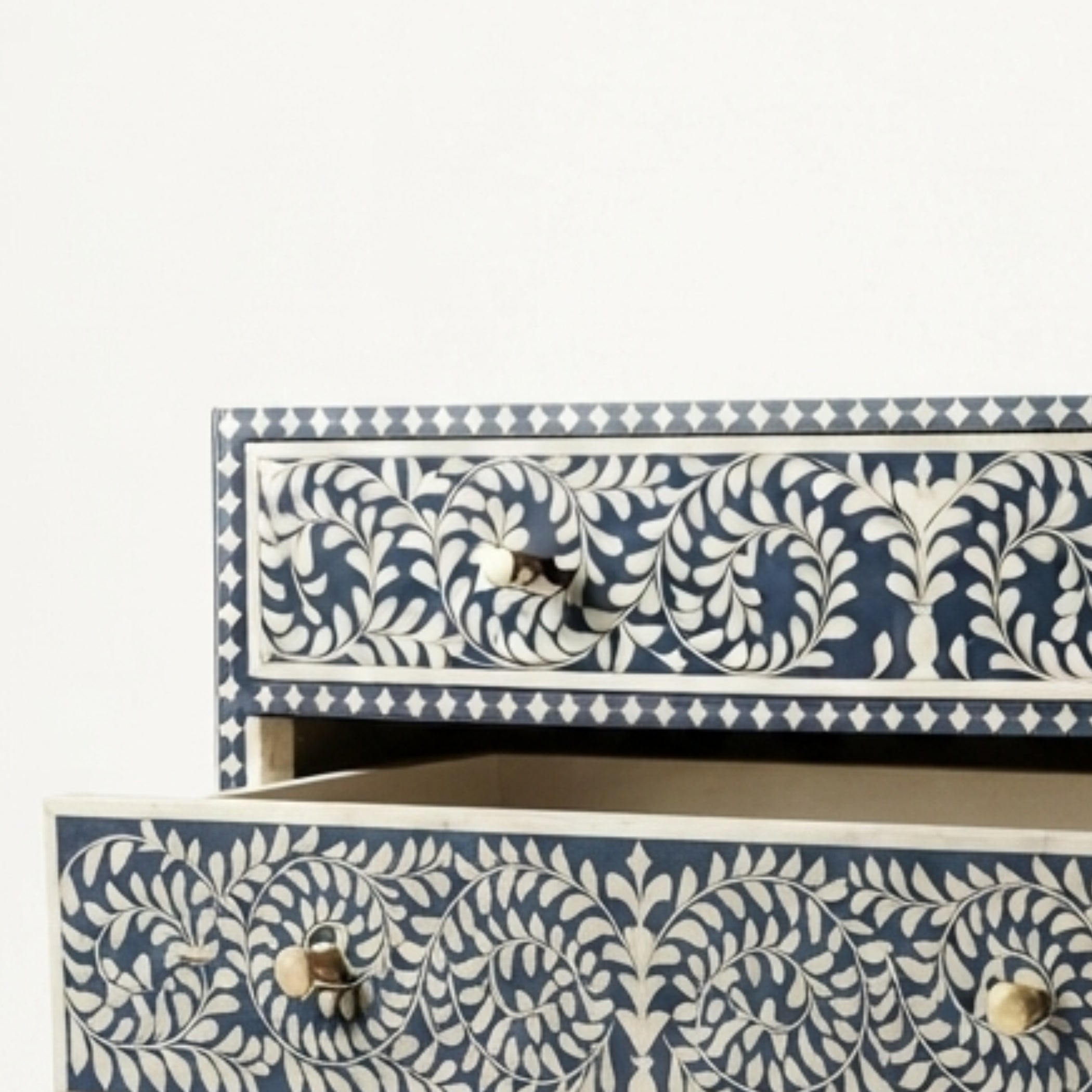 Close-up of a decorative drawer with a navy blue and off-white floral bone-inlay pattern, featuring a small metal pull handle and a light wood drawer front.