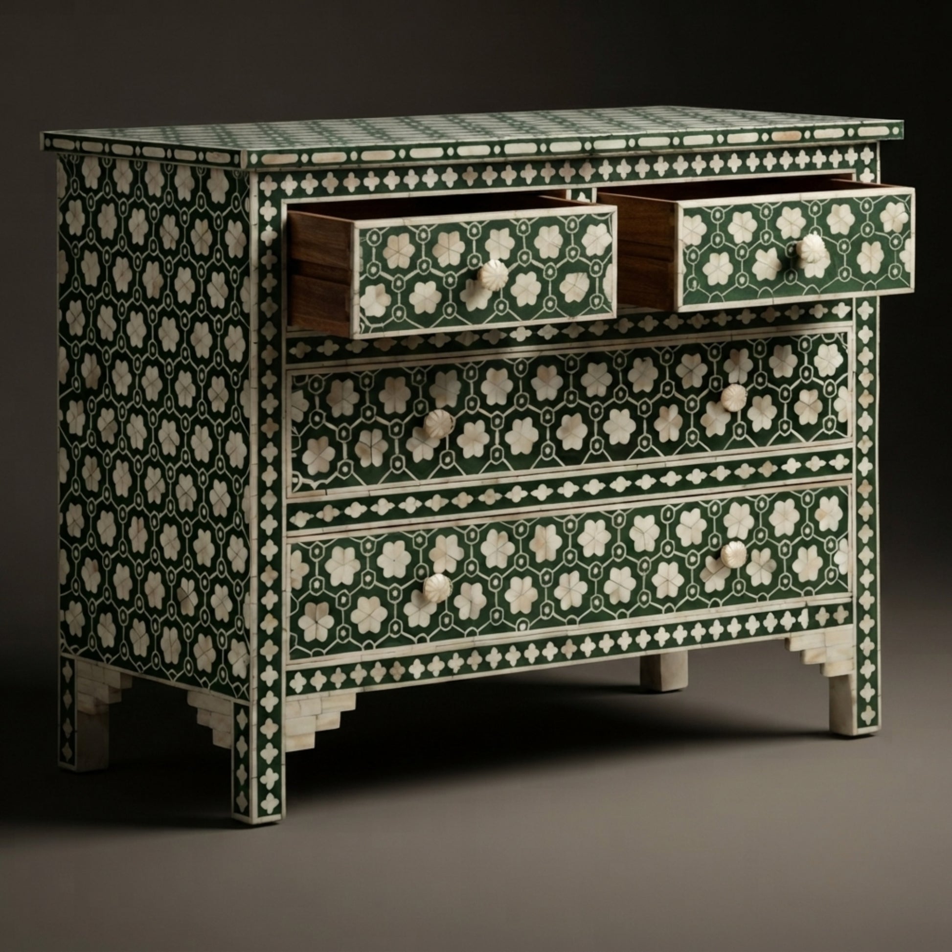 An ornate three-drawer chest with intricate green and ivory bone-inlay patterns, featuring two open drawers on top and decorative drawer pulls, set against a dark studio background.