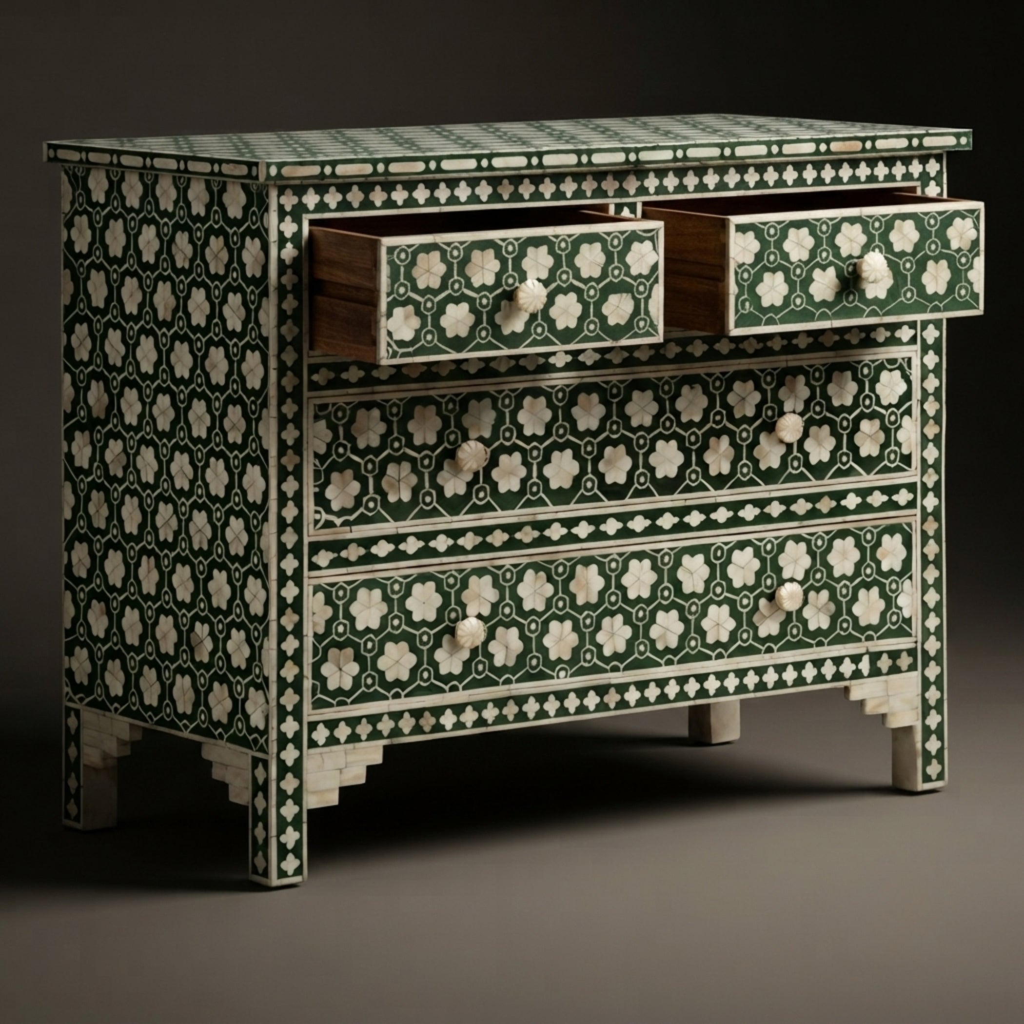 An ornate three-drawer chest with intricate green and ivory bone-inlay patterns, featuring two open drawers on top and decorative drawer pulls, set against a dark studio background.