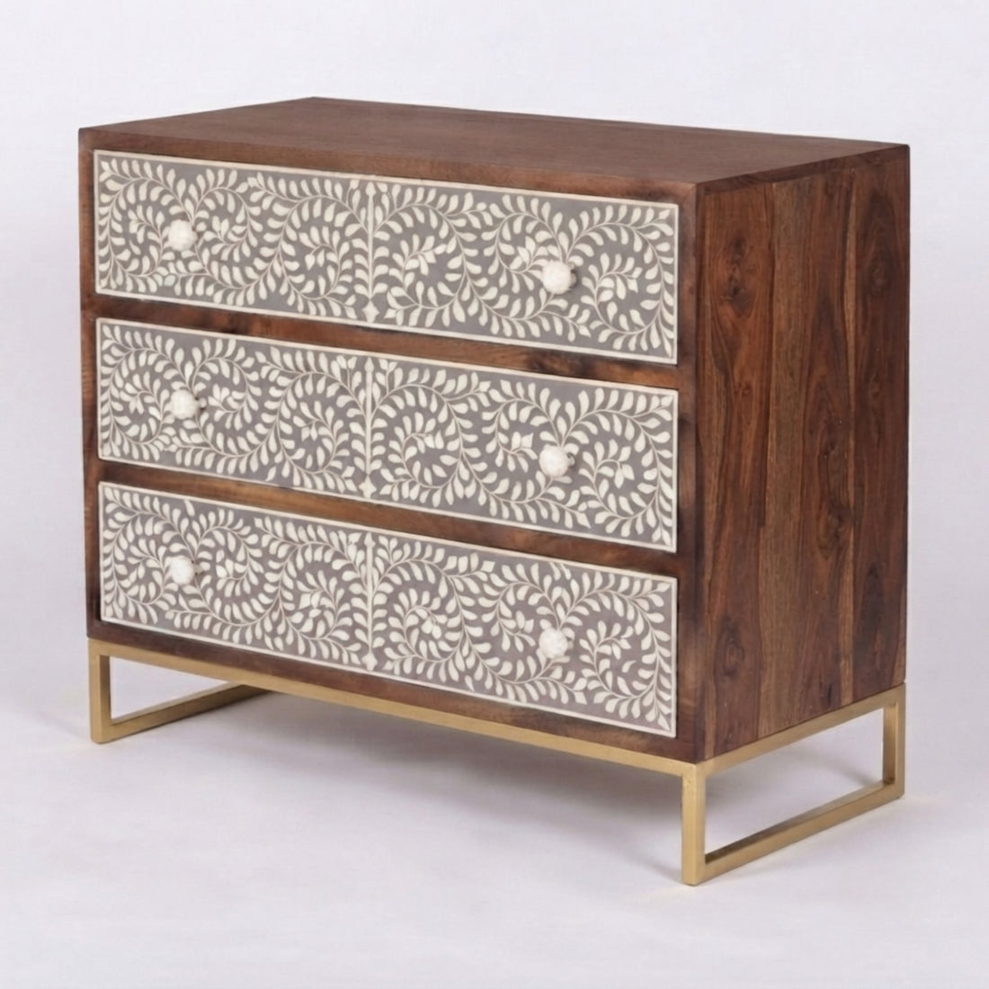 A three-drawer chest of drawers with a dark wood frame, bone-patterned drawer fronts, and gold legs, styled in a home interior setting with decorative items on top.