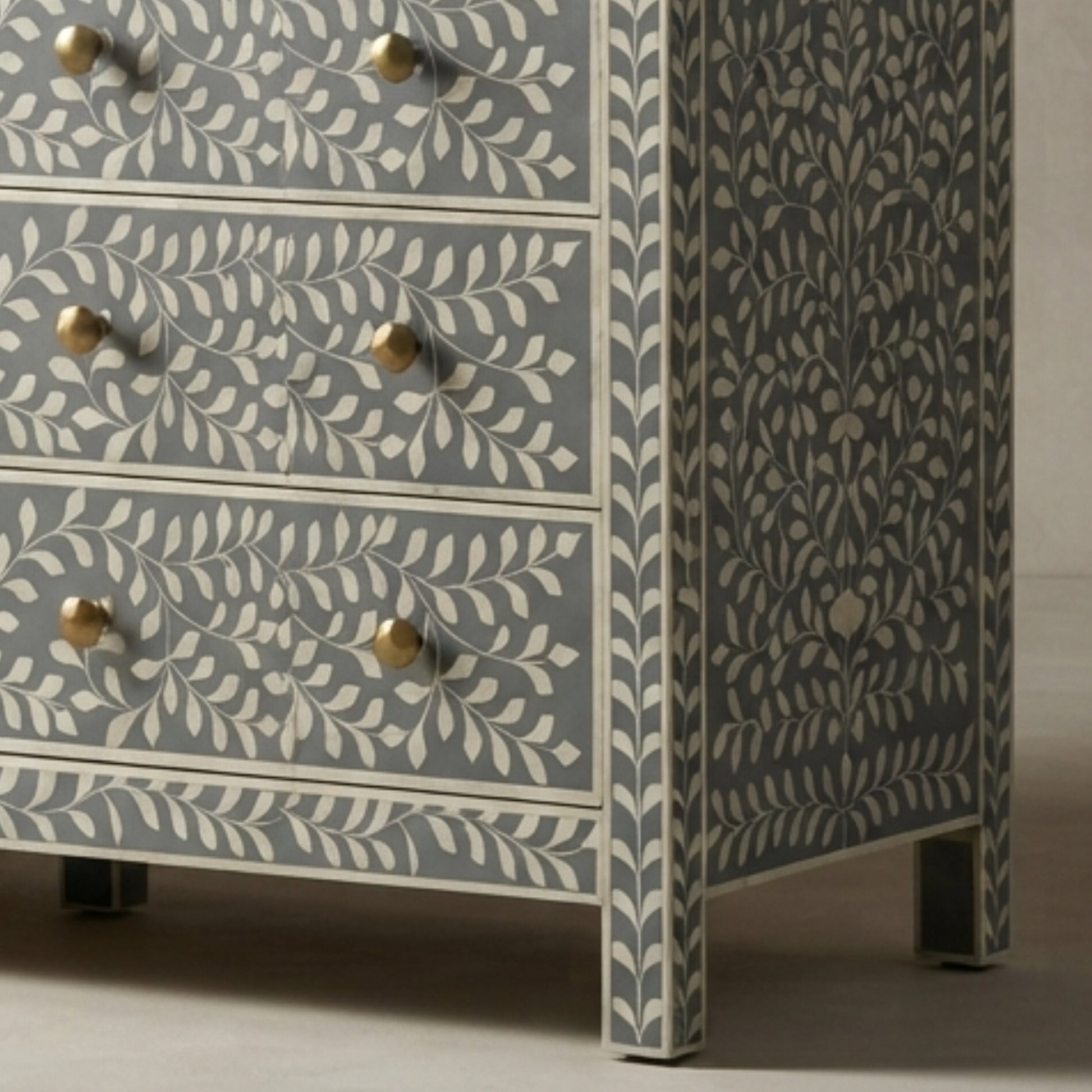 A close-up of a chest of drawers with a blue-gray and cream bone-in-laminate pattern, featuring brass knobs and dark metal feet.