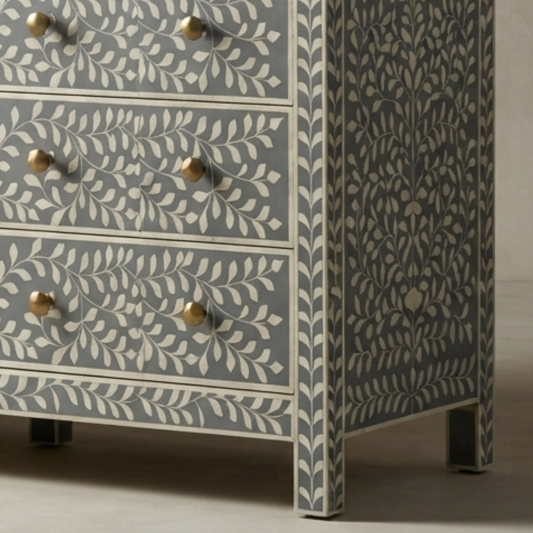 A close-up of a chest of drawers with a blue-gray and cream bone-in-laminate pattern, featuring brass knobs and dark metal feet.