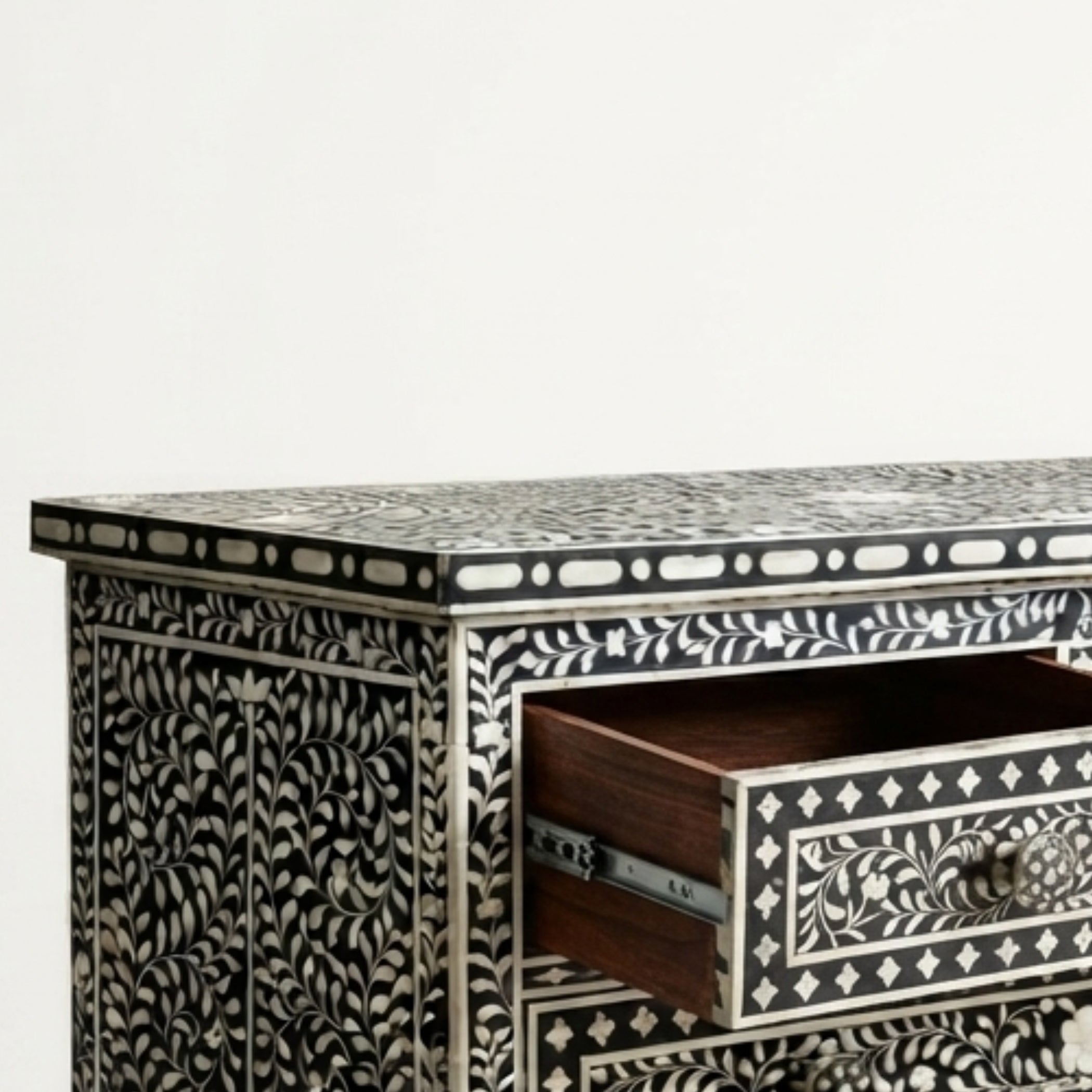 A close-up of an ornate black and white bone-inlay cabinet with a single open drawer showing a dark wood interior, set against a plain light background.