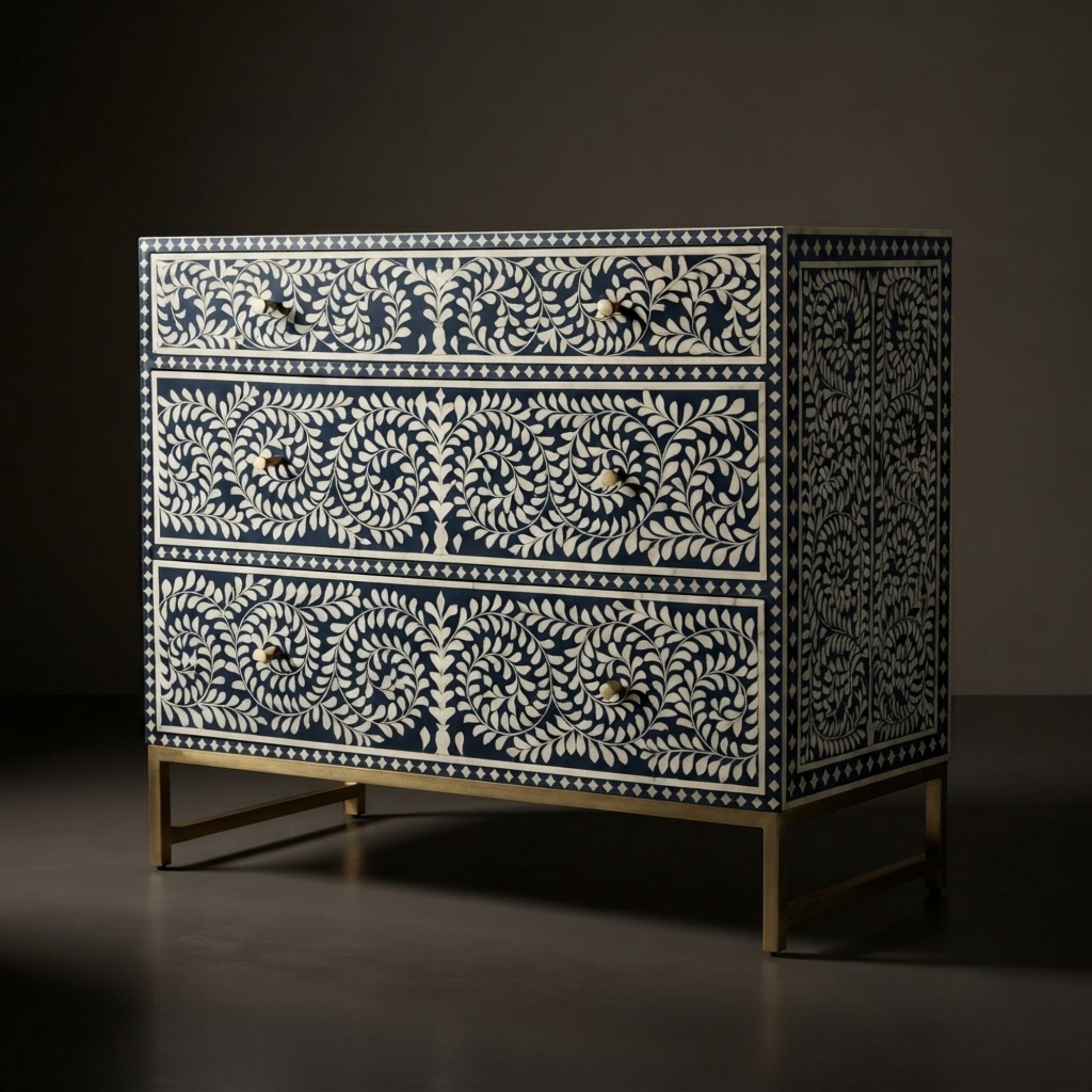 A three-drawer chest of drawers featuring an intricate bone-inlay pattern in cream and navy blue, with small brass knobs and a slim brass metal frame.