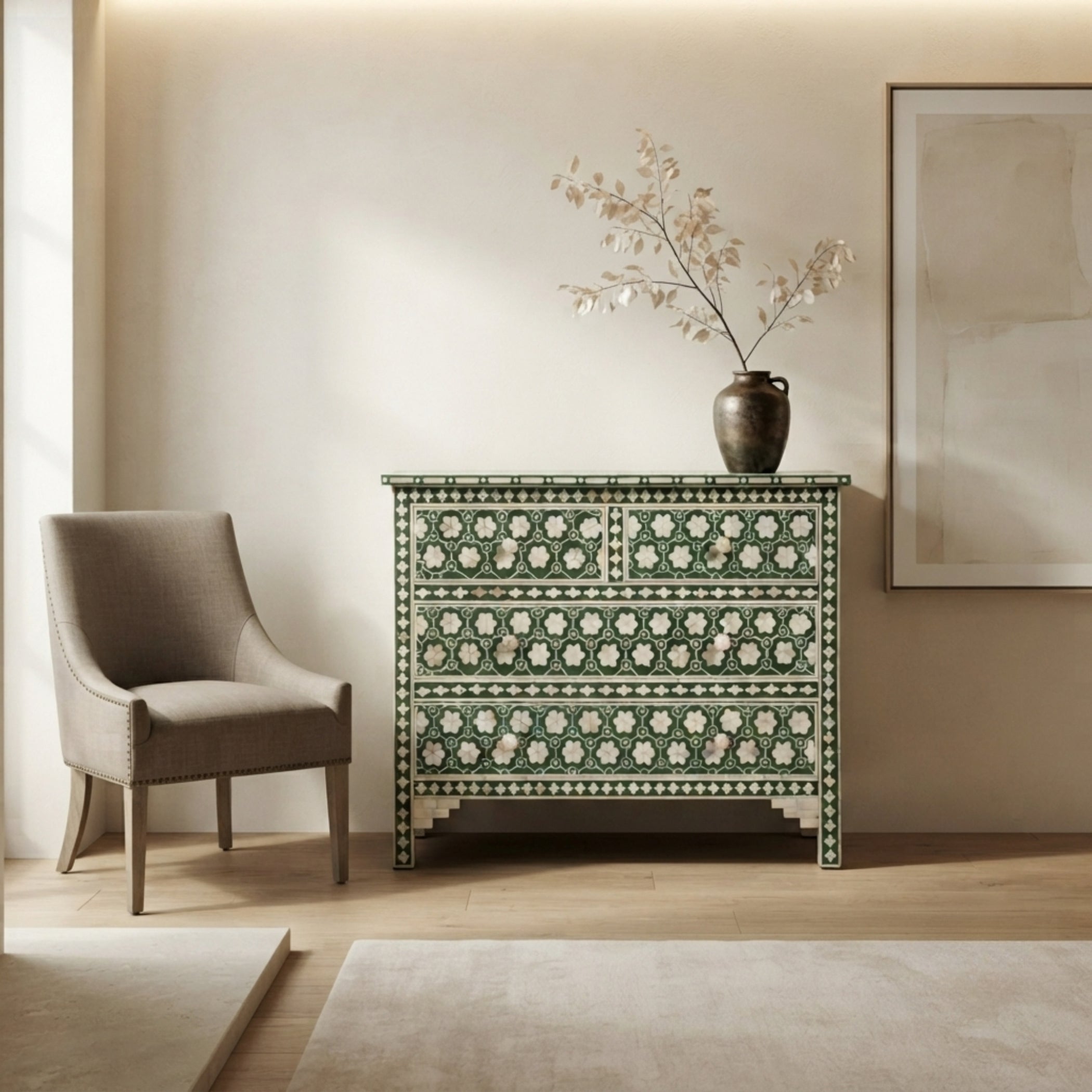 A green and white patterned wooden chest of drawers styled in a warm, minimalist room next to a beige armchair, with a dark ceramic vase holding dried branches on top.
