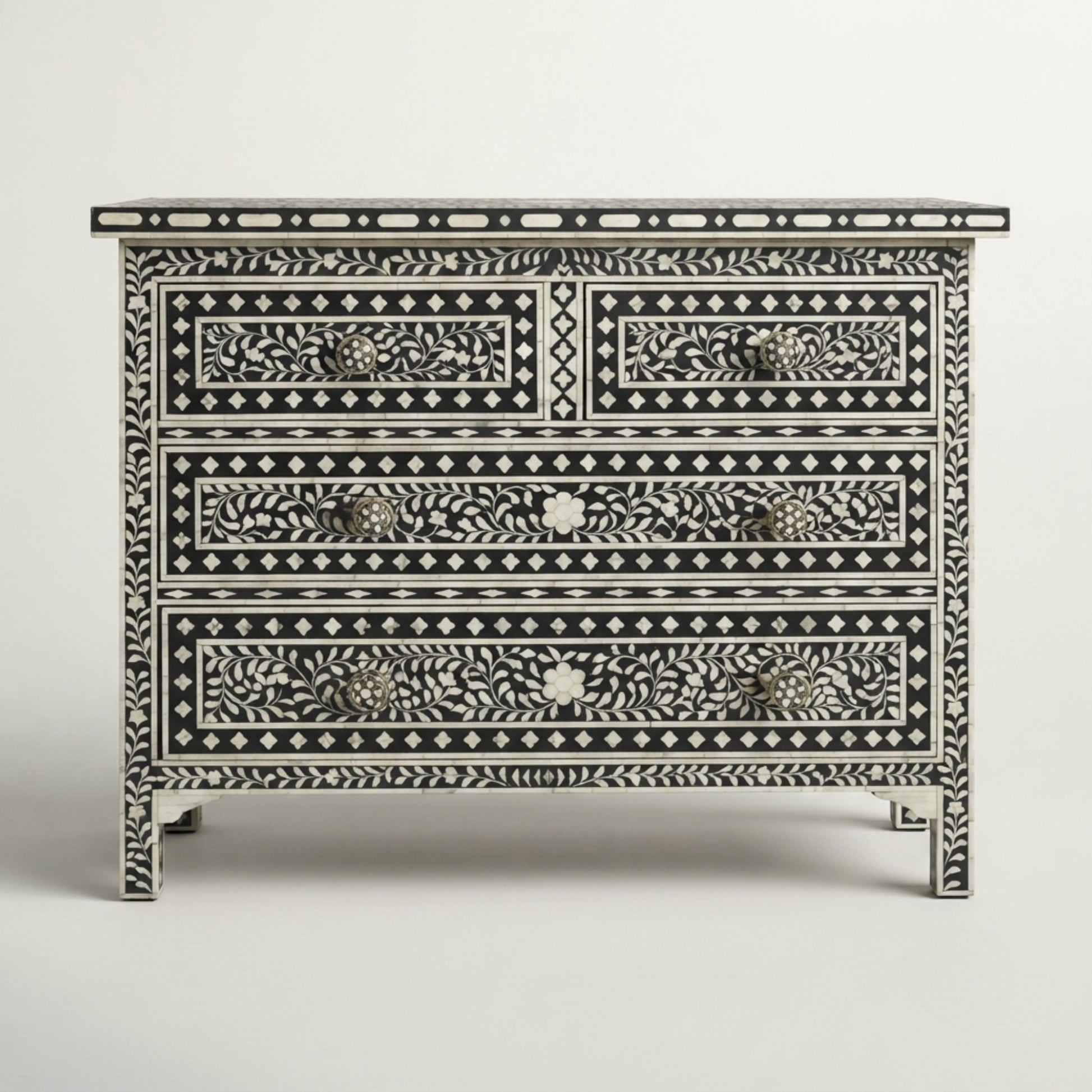 A three-drawer chest of drawers featuring intricate black and white bone-inlay floral and geometric patterns, with small brass drawer pulls, set against a neutral light gray background.