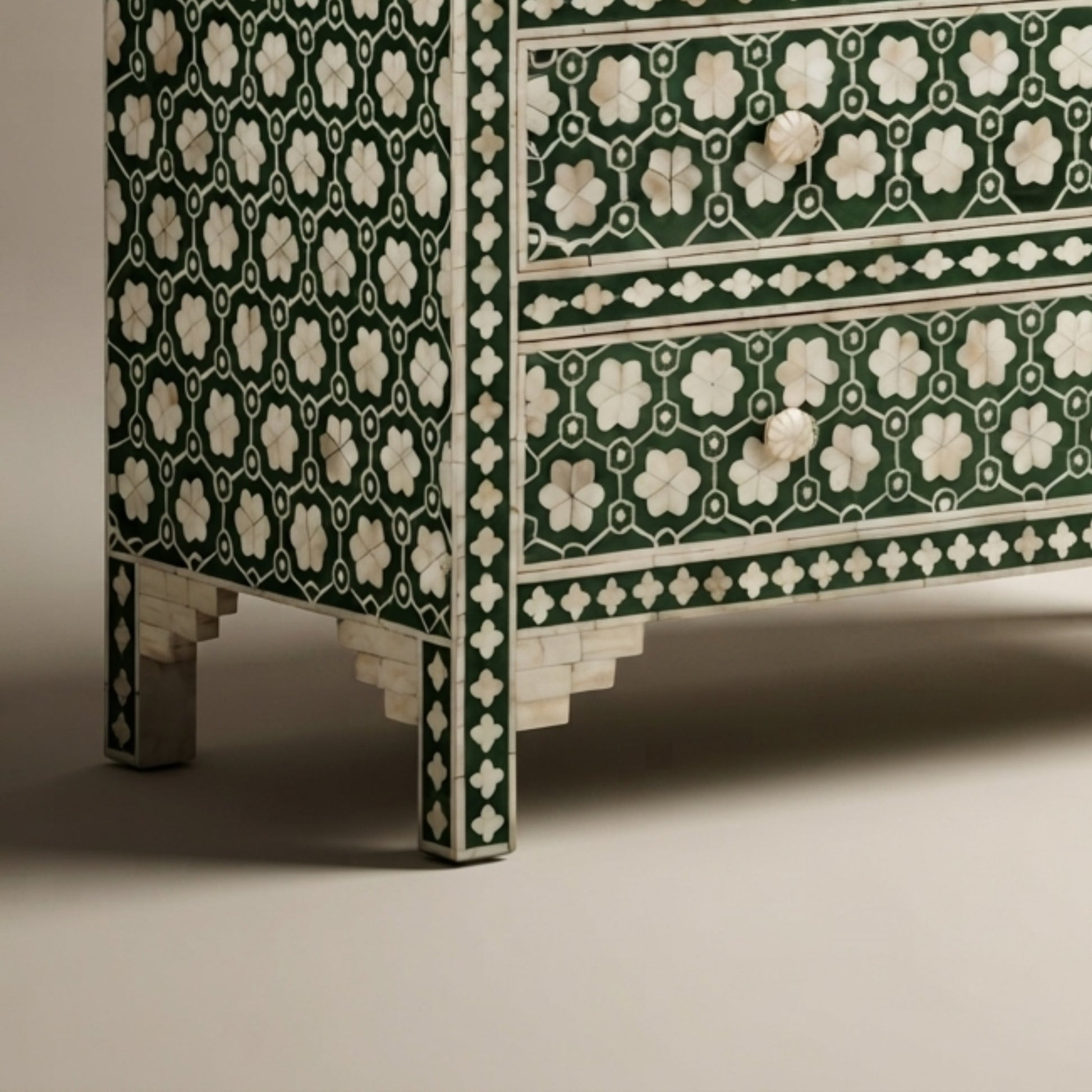 Close-up of a decorative chest of drawers with a dark green and white floral inlay pattern, featuring three drawers and ornate legs on a neutral studio background.