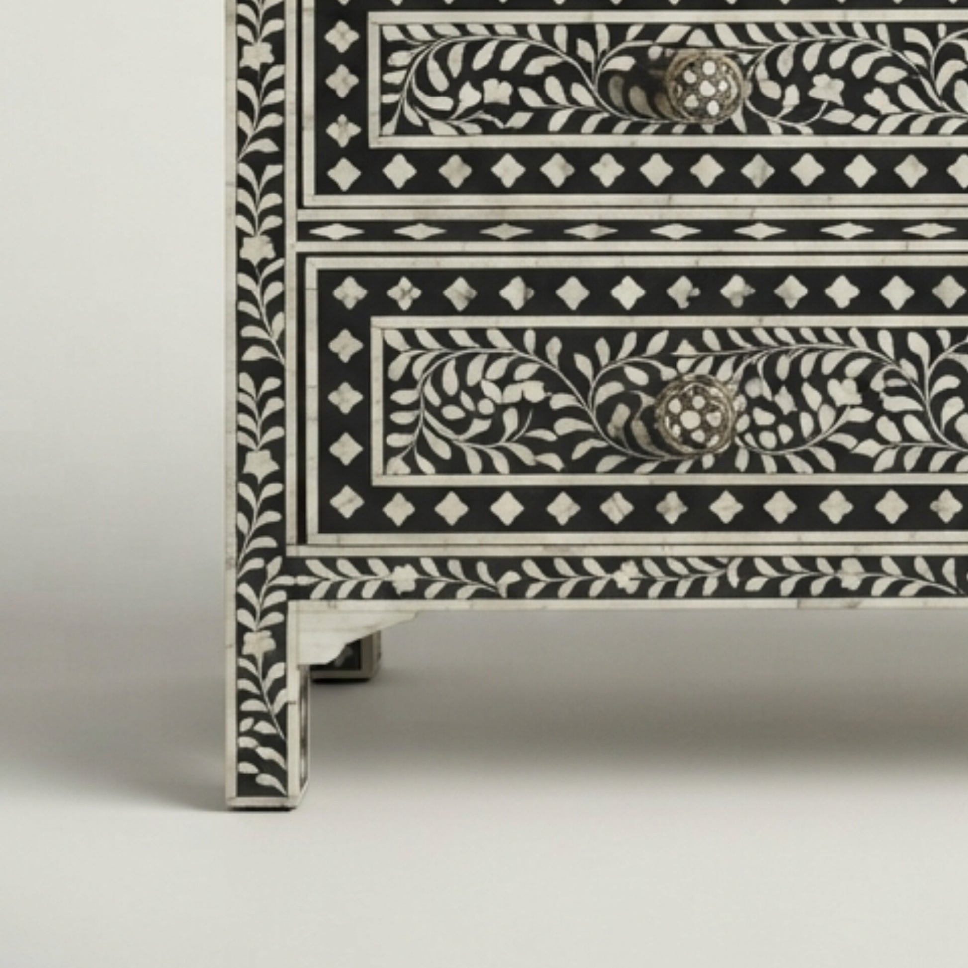 Close-up of a black and white bone-inlay chest of drawers showing detailed floral patterns and textured drawer pulls on a light gray background.