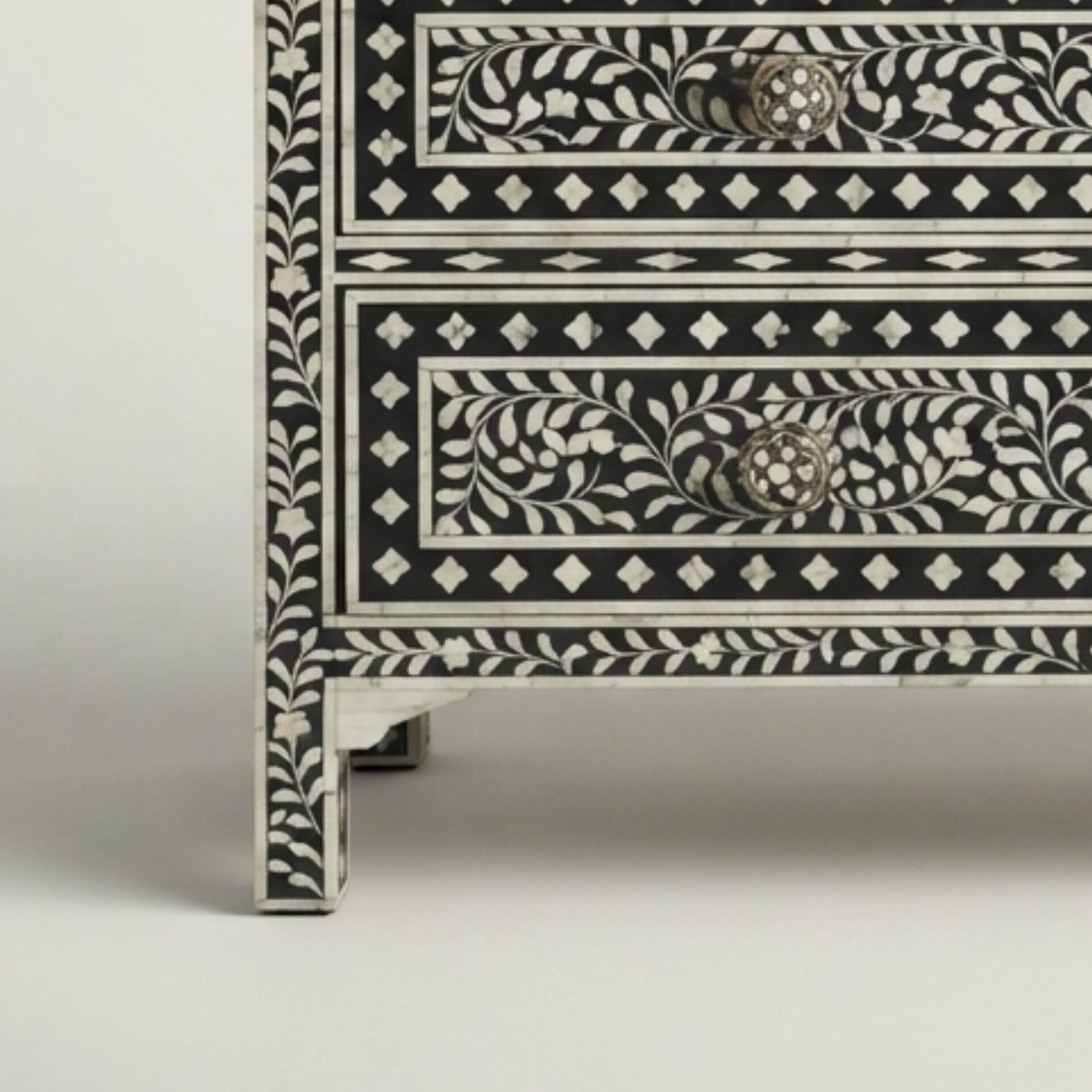Close-up of a black and white bone-inlay chest of drawers showing detailed floral patterns and textured drawer pulls on a light gray background.