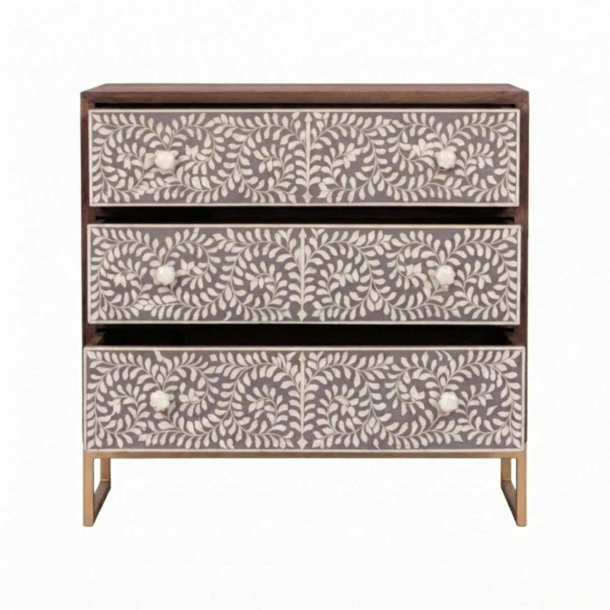 A three-drawer chest of drawers with a dark brown wood frame and bone-inlay panels featuring a cream floral and leaf pattern, supported by slim gold-toned legs.