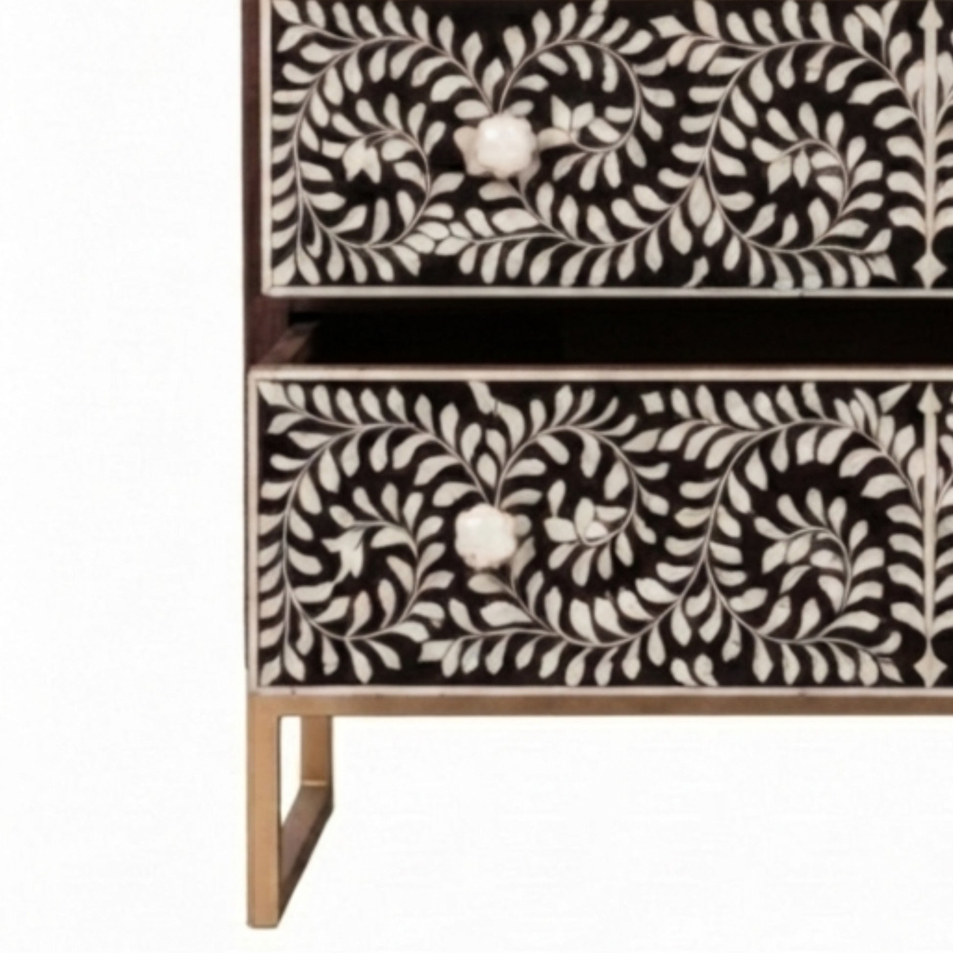 A close-up of a two-drawer chest or cabinet with black and white floral bone-inlay panels and small metallic legs, shown against a plain white background.