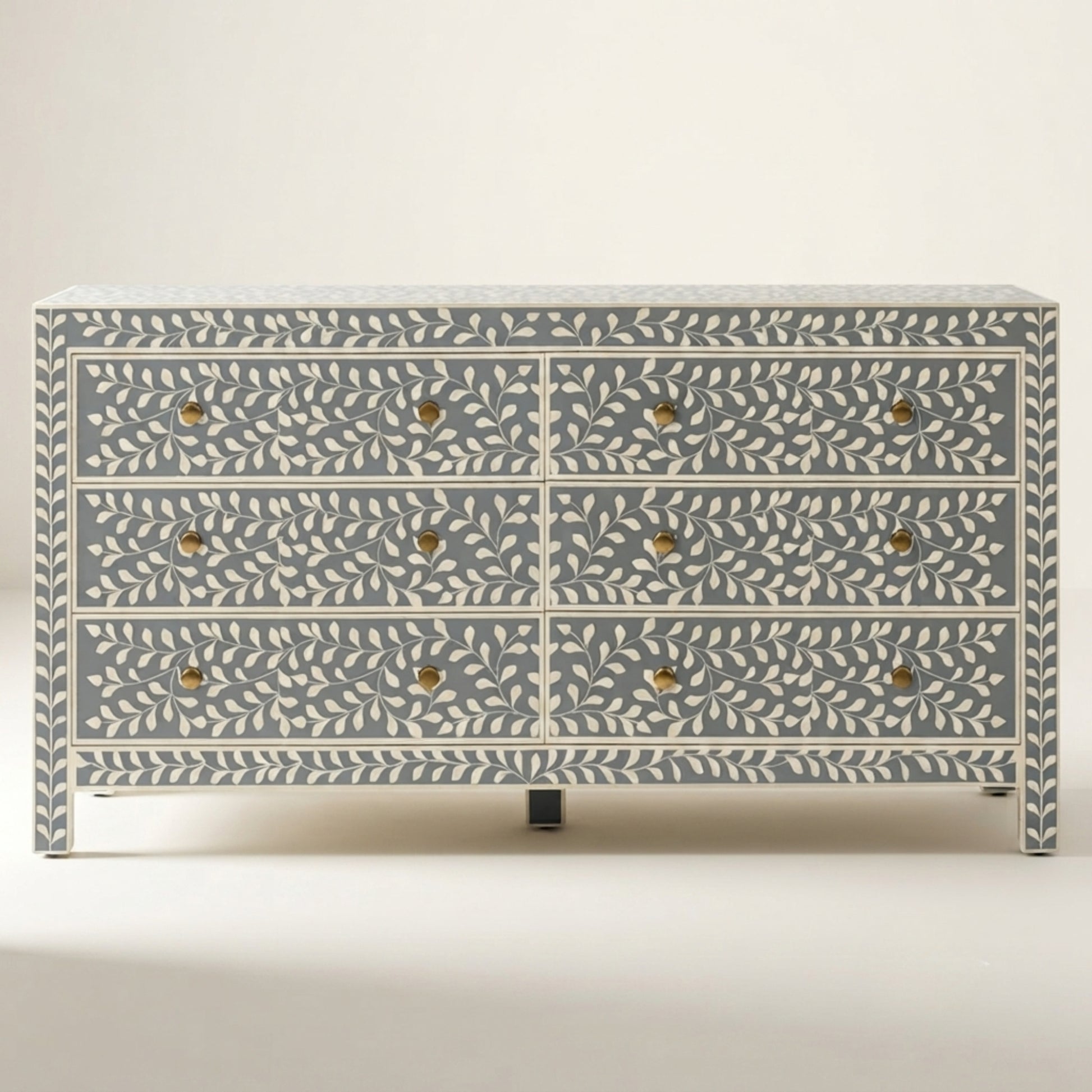 A six-drawer chest of drawers featuring a blue-gray and white bone-inlay leaf pattern with small gold-toned metal knobs, set against a plain light beige background.