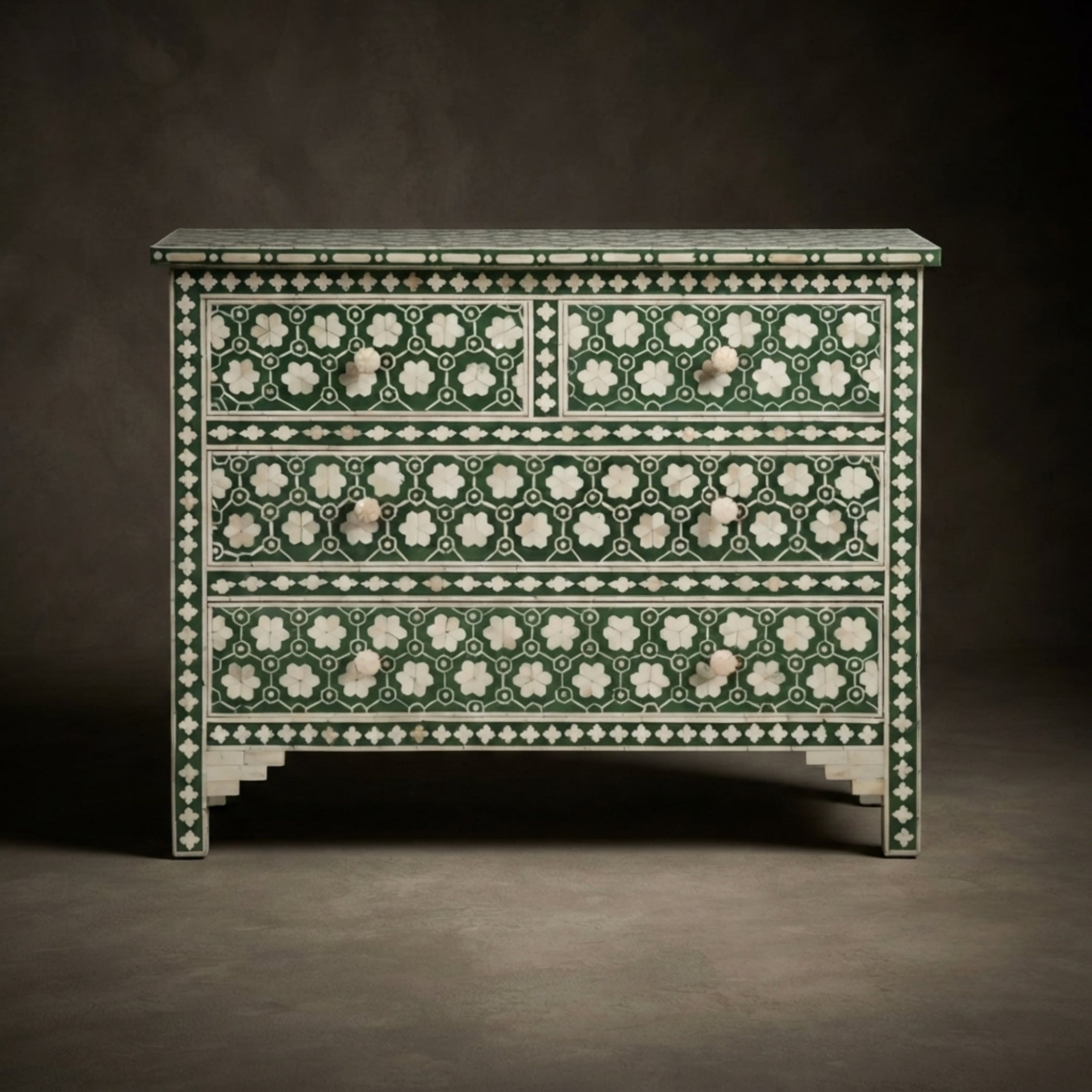 An ornate three-drawer chest with intricate green and white bone-inlay patterns, set against a dark gray studio background.