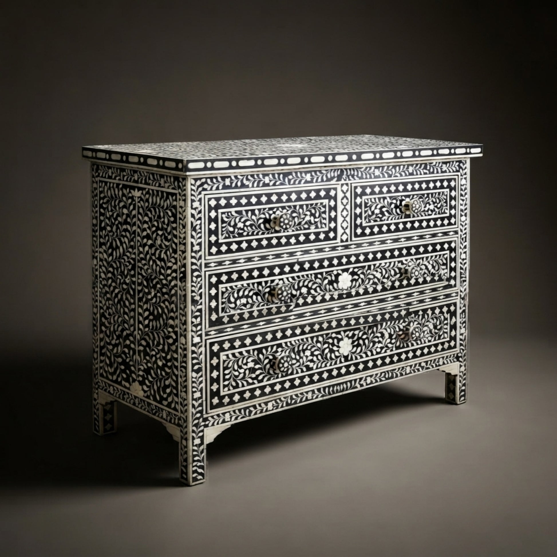 A three-drawer chest of drawers featuring intricate black and white bone-inlay patterns, photographed against a dark gray studio background.