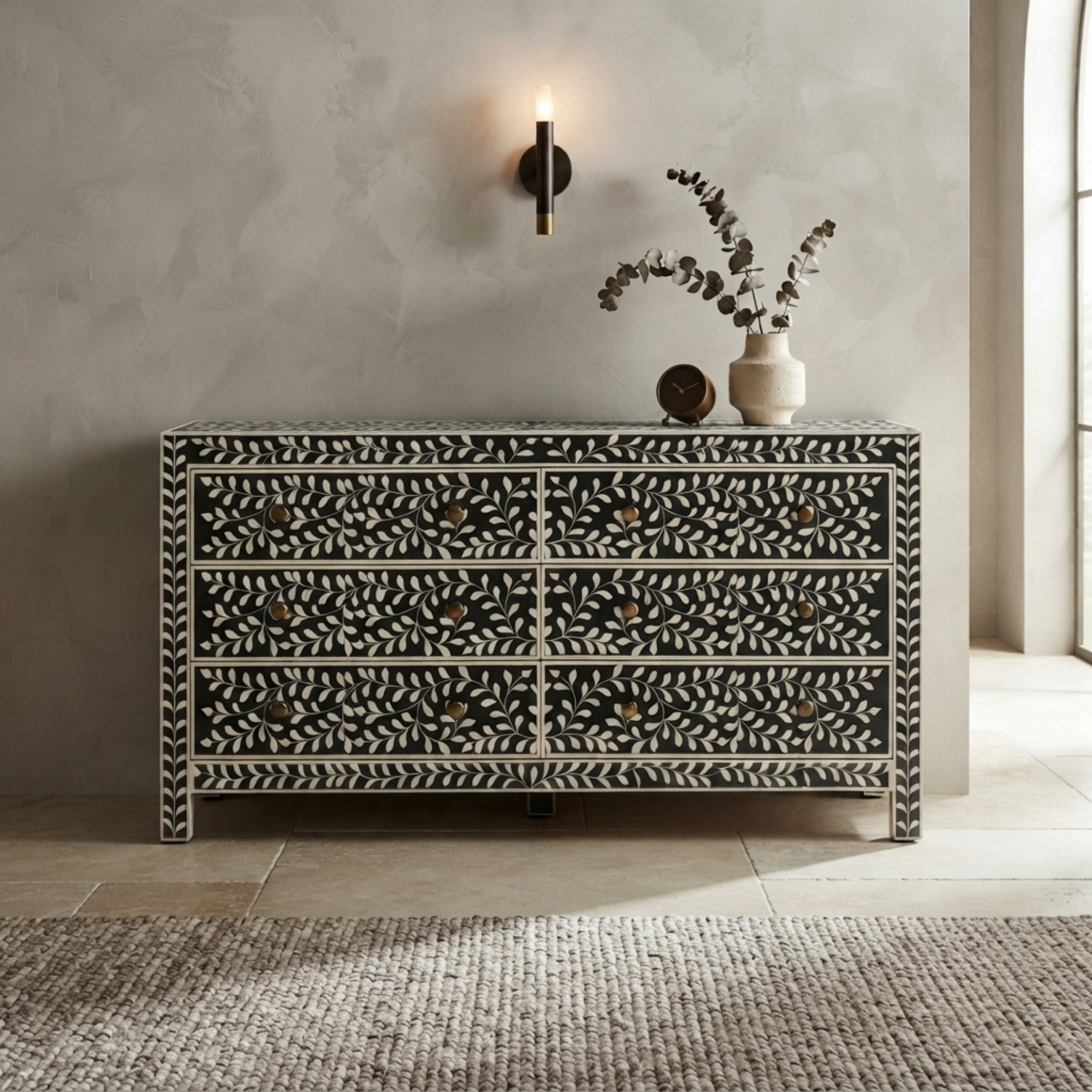 A black and white patterned bone-in-wood chest of drawers with six drawers, styled in a modern room setting with a wall sconce, vase, and rug.