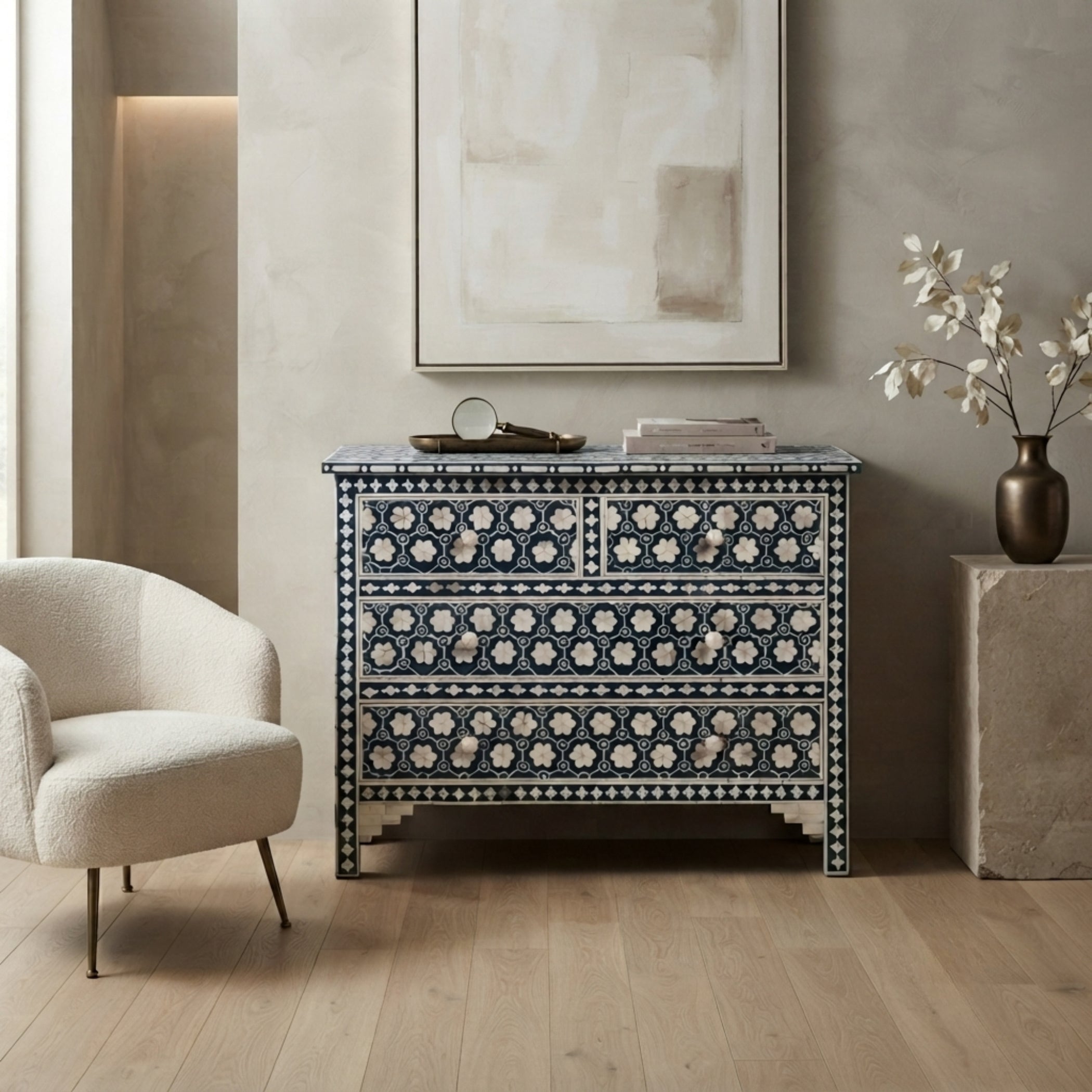A blue and white patterned chest of drawers styled in a modern living room setting with a cream armchair, a textured wall, and a vase of white flowers.