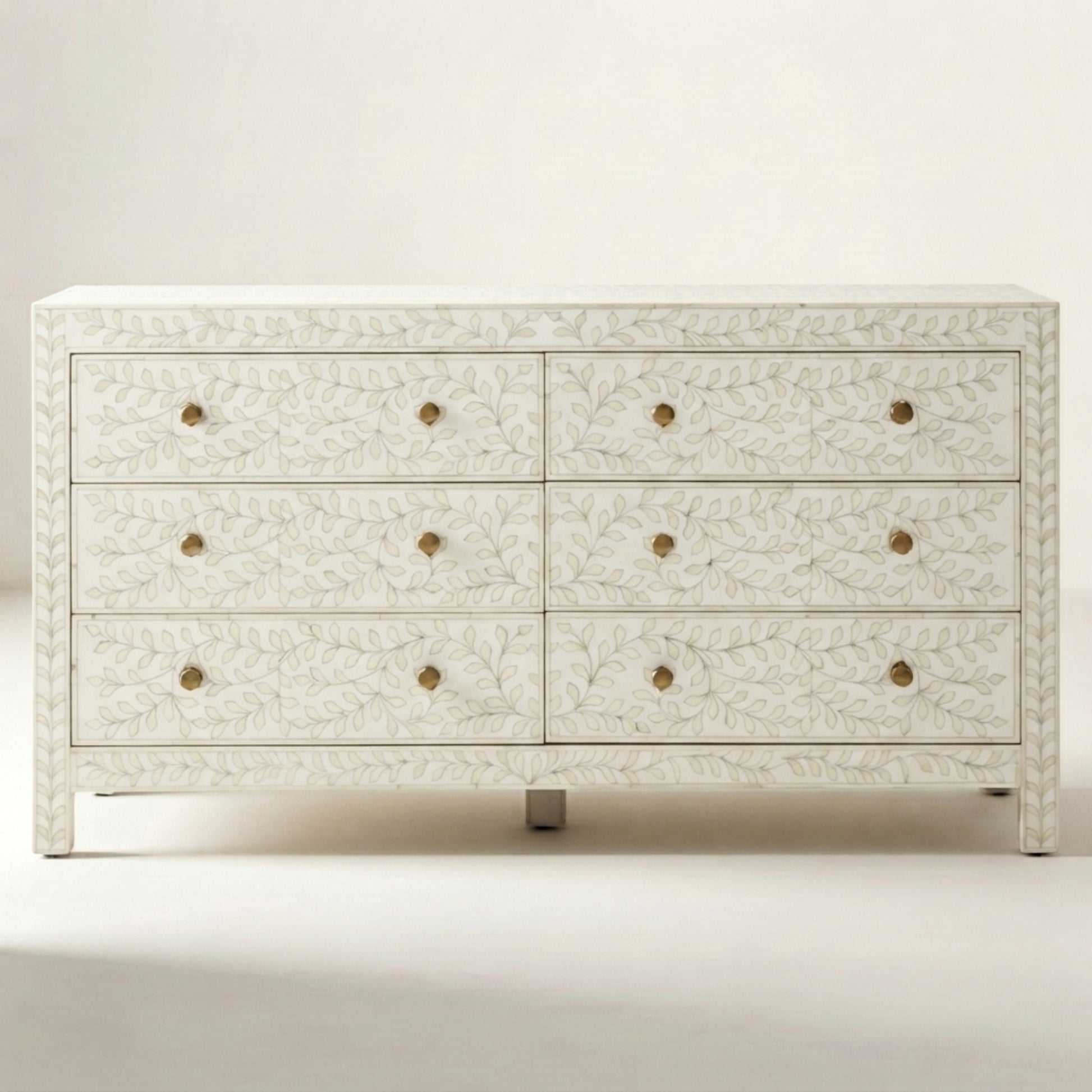 An eight-drawer dresser with an ivory carved floral pattern and small brass round knobs, shown against a neutral cream background.