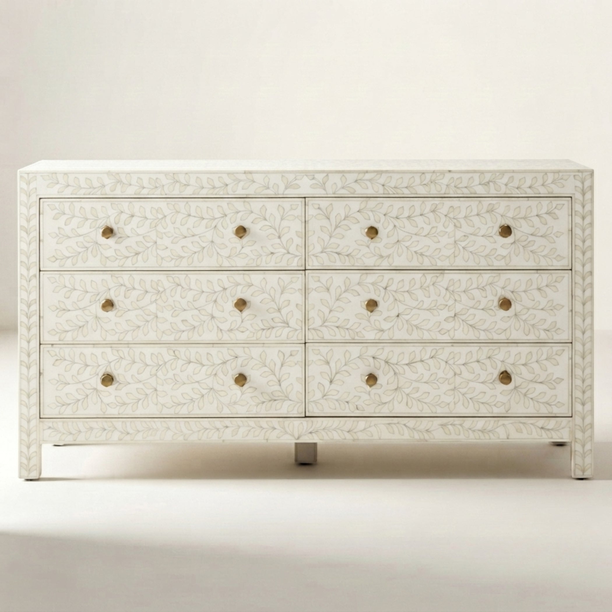 An eight-drawer dresser with an ivory carved floral pattern and small brass round knobs, shown against a neutral cream background.