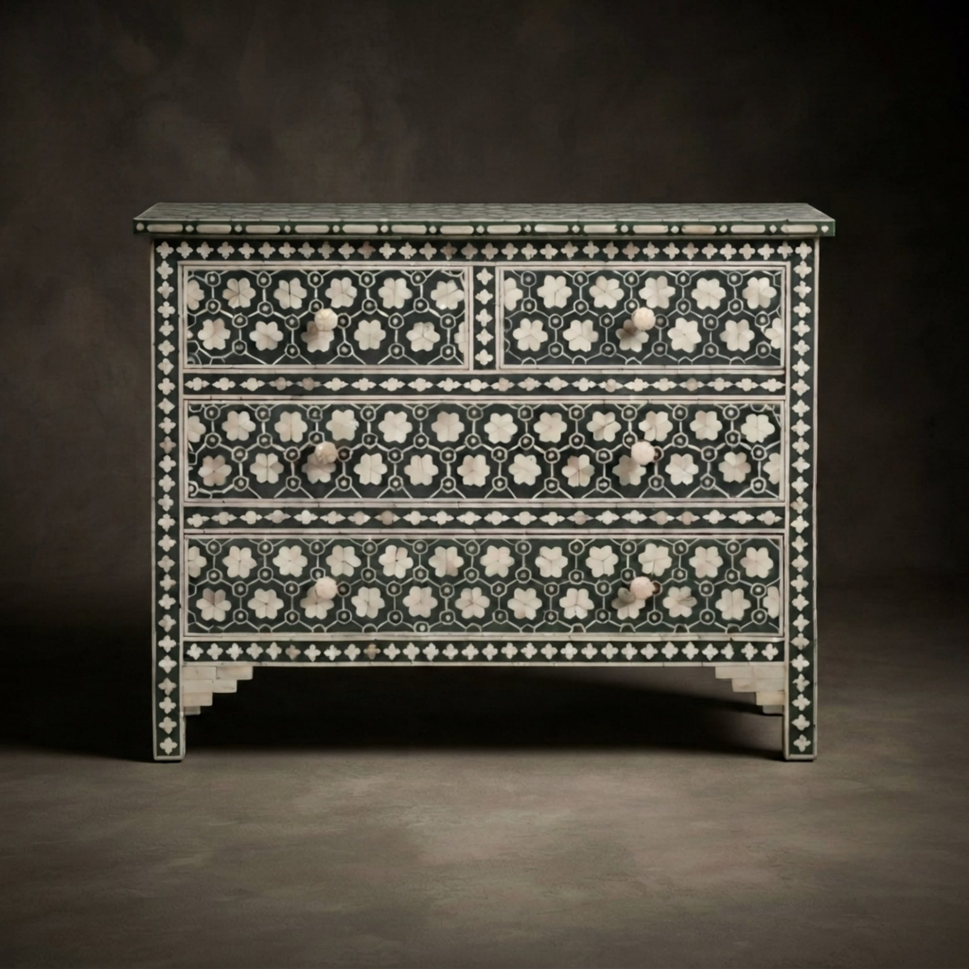 An ornate three-drawer chest or dresser featuring intricate black and white bone-inlay patterns, set against a dark, neutral studio background.