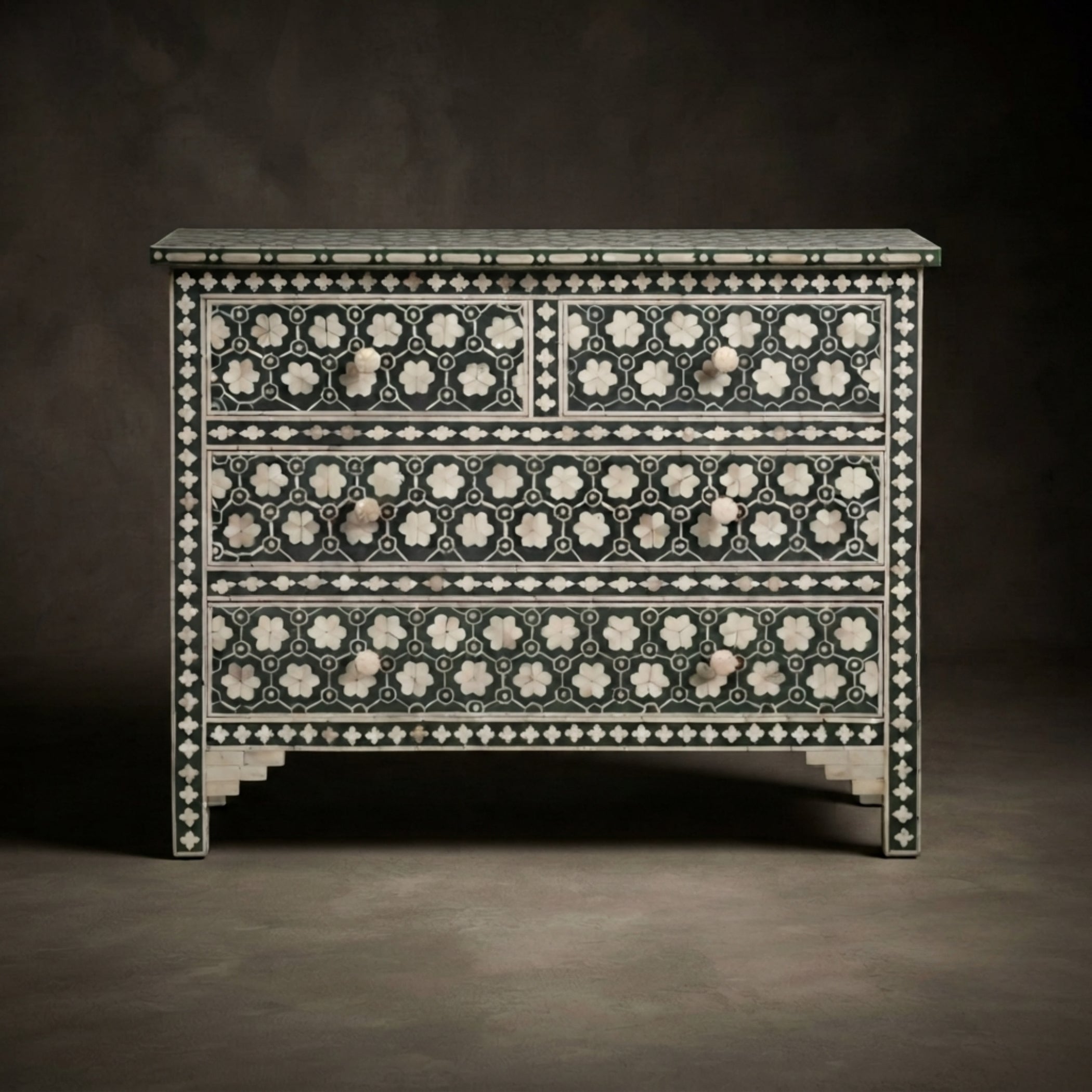 An ornate three-drawer chest or dresser featuring intricate black and white bone-inlay patterns, set against a dark, neutral studio background.
