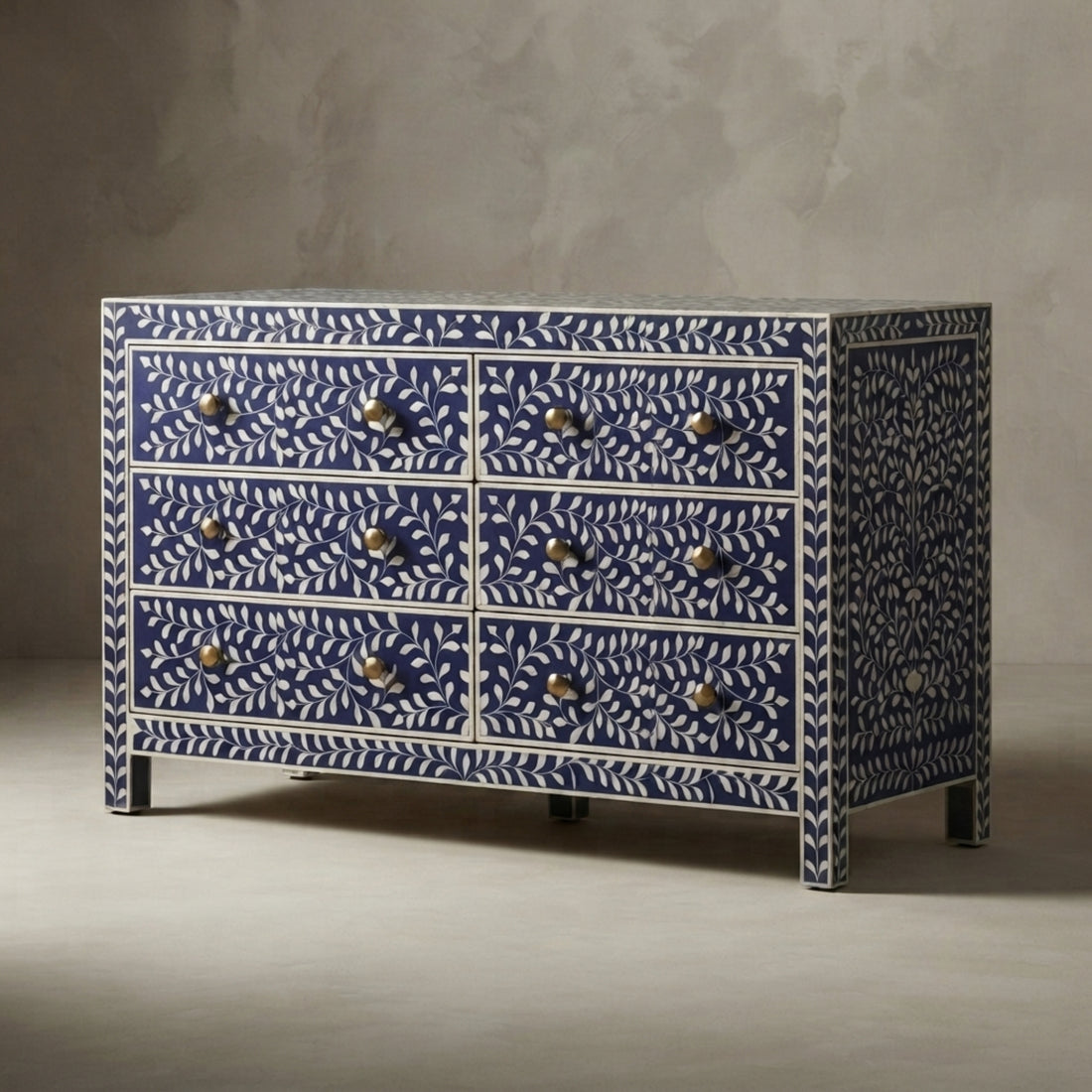 A navy blue and white patterned sideboard or dresser with multiple drawers, styled in a minimalist room with a vase of dried leaves, books, and a wall sconce.