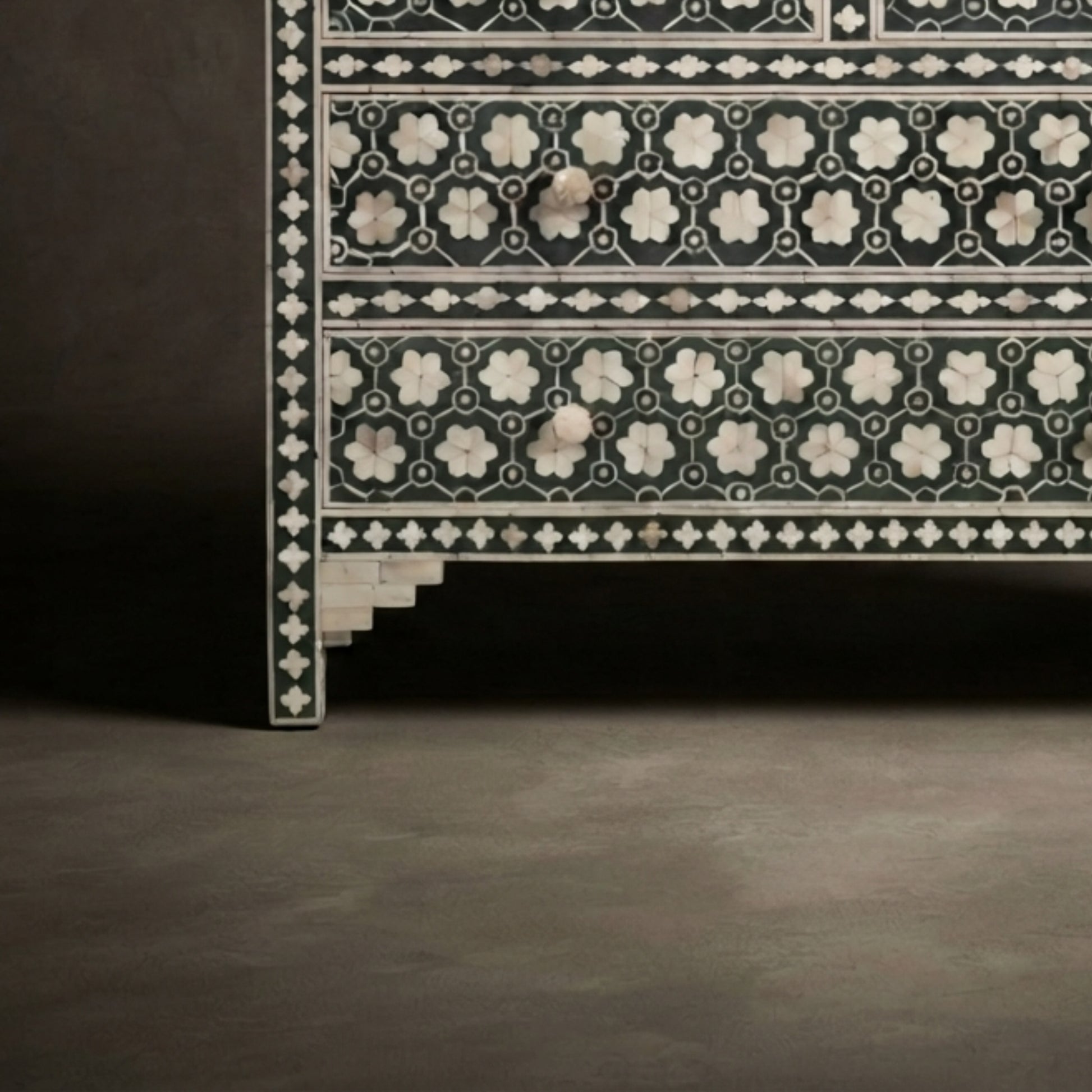 Close-up of an ornate black and white inlaid wooden cabinet or chest with geometric and floral patterns, set against a dark studio background.