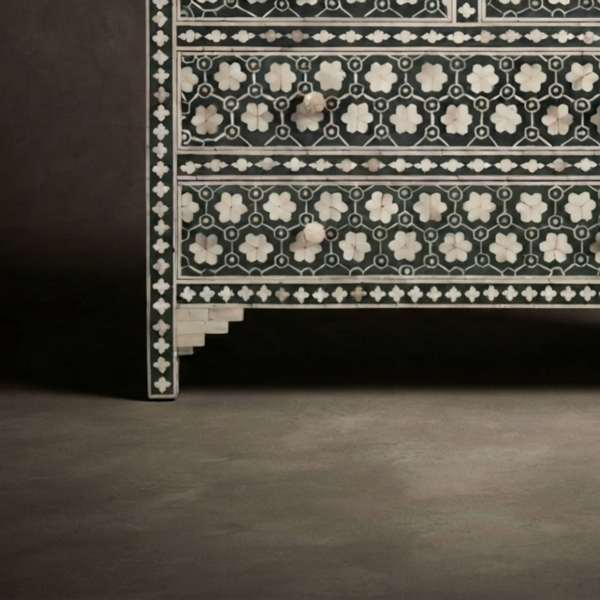 Close-up of an ornate black and white inlaid wooden cabinet or chest with geometric and floral patterns, set against a dark studio background.
