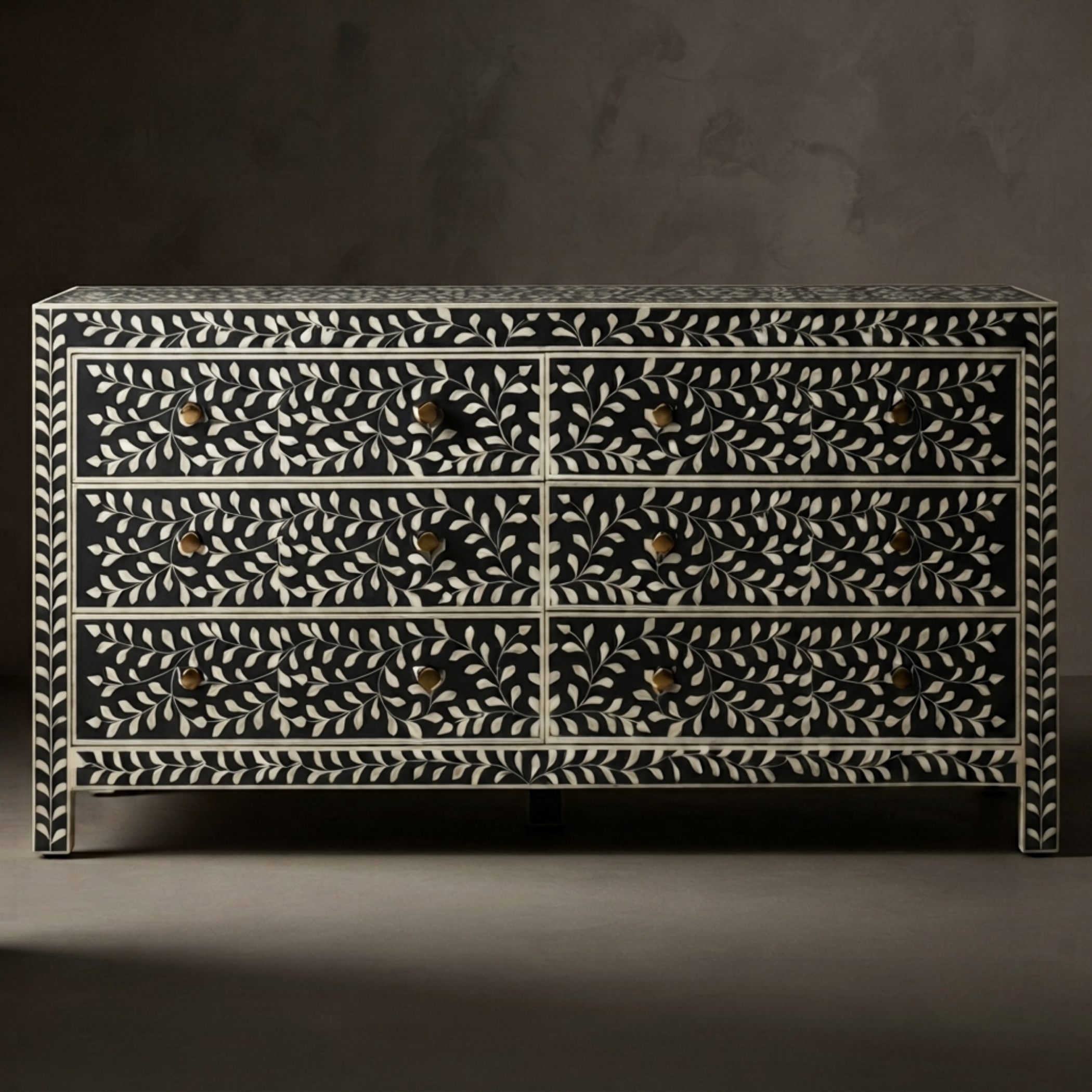 A six-drawer dresser with an intricate black and white bone-inlay leaf pattern and small brass knobs, set against a dark gray background.