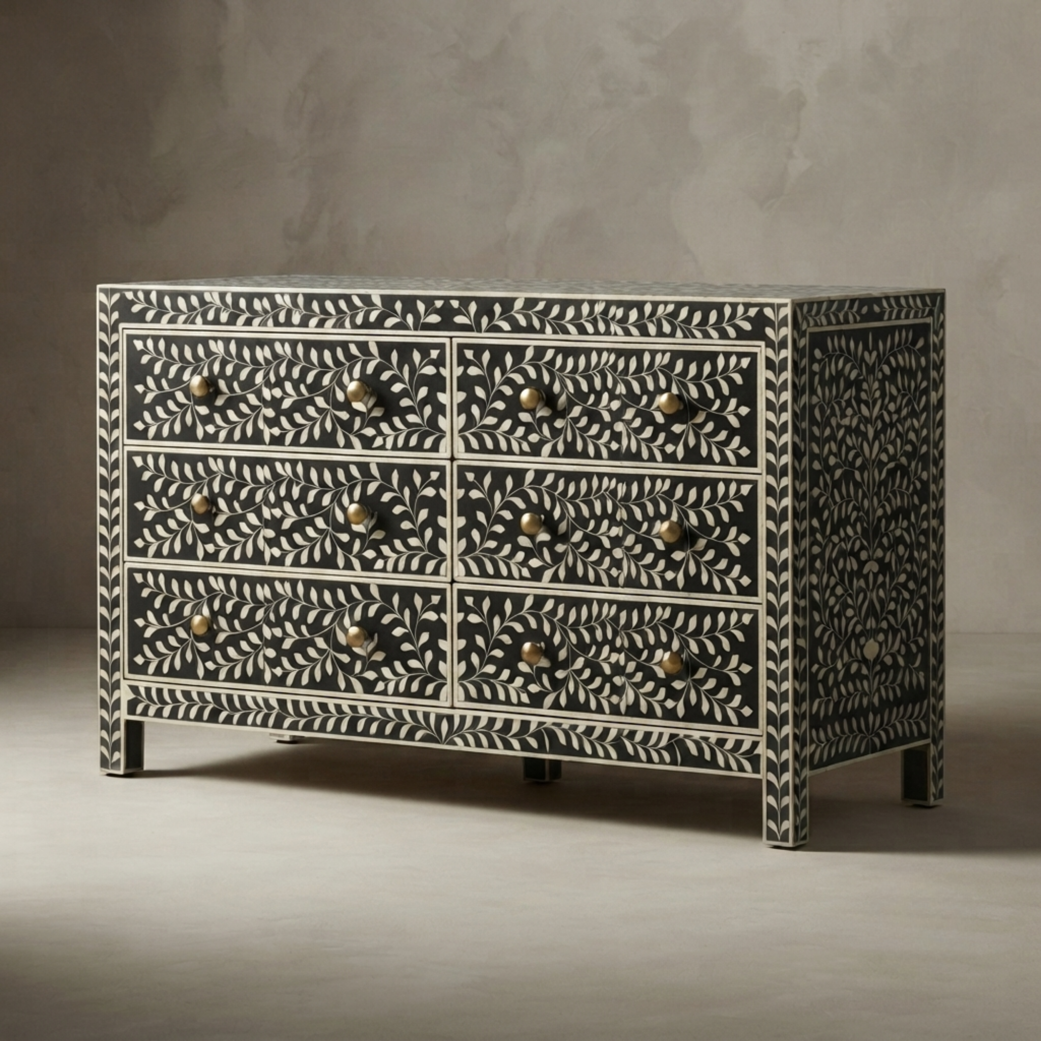 A six-drawer chest of drawers featuring an intricate black and white bone-in-wood style floral pattern, with small round brass knobs, set against a neutral gray textured background.