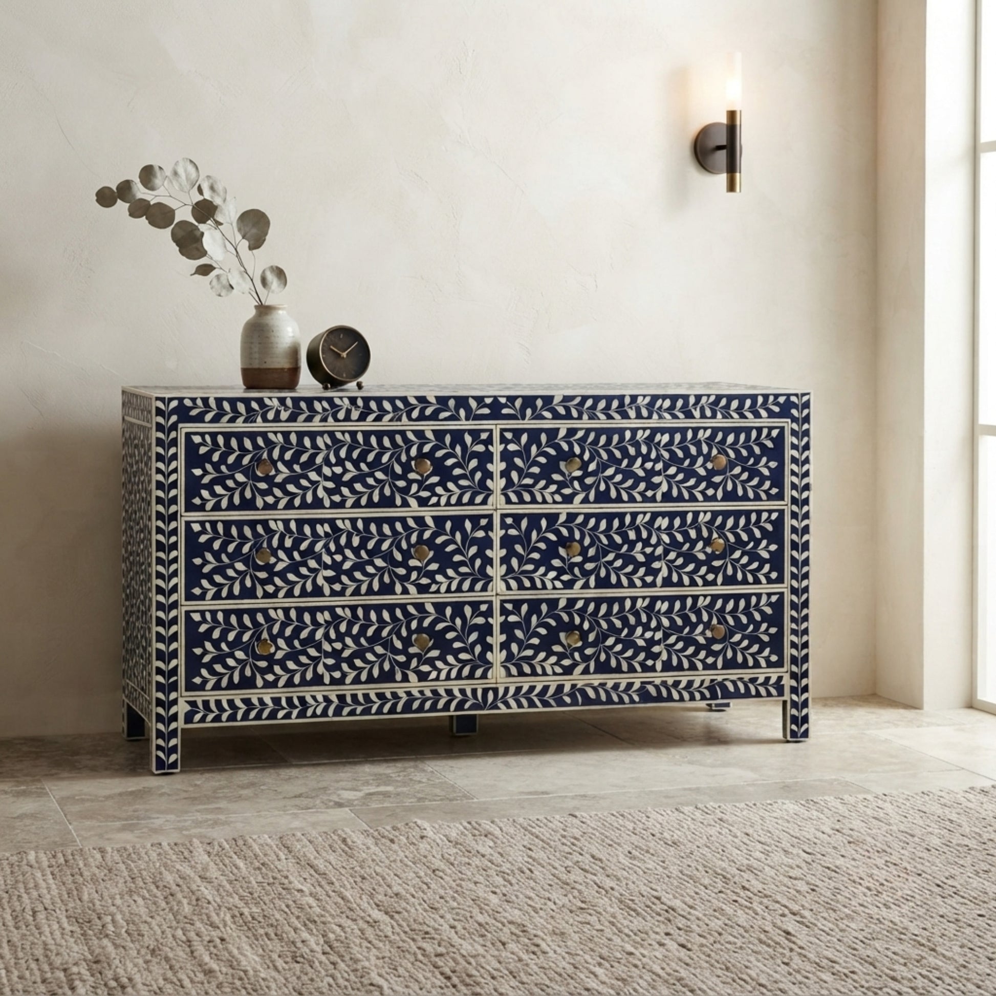 A six-drawer chest of drawers with a navy blue and white bone-inlay pattern, styled in a modern room setting with a vase and clock on top.
