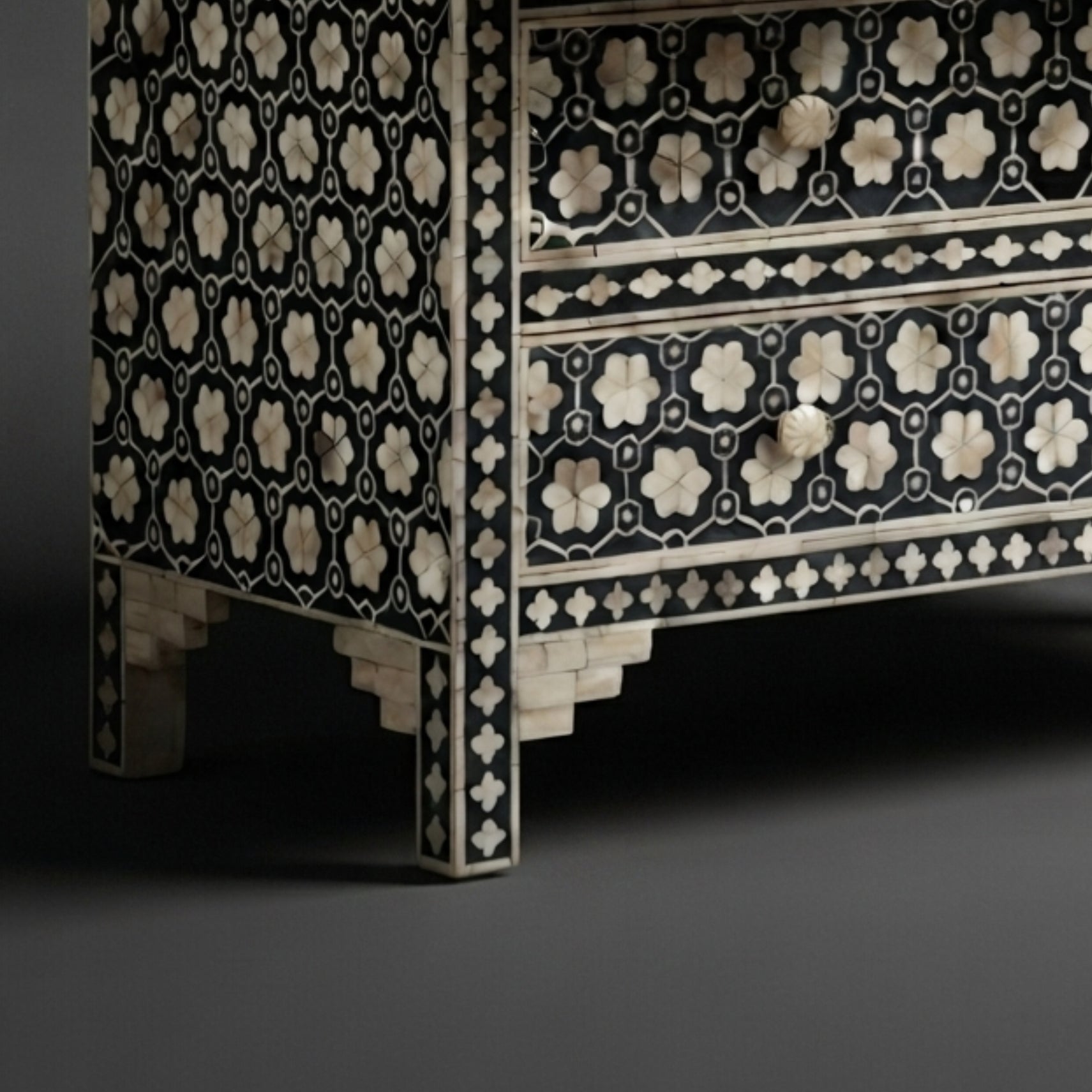 A close-up of an ornate black and ivory inlaid wooden cabinet or chest with geometric and floral patterns, shown against a dark gray background.