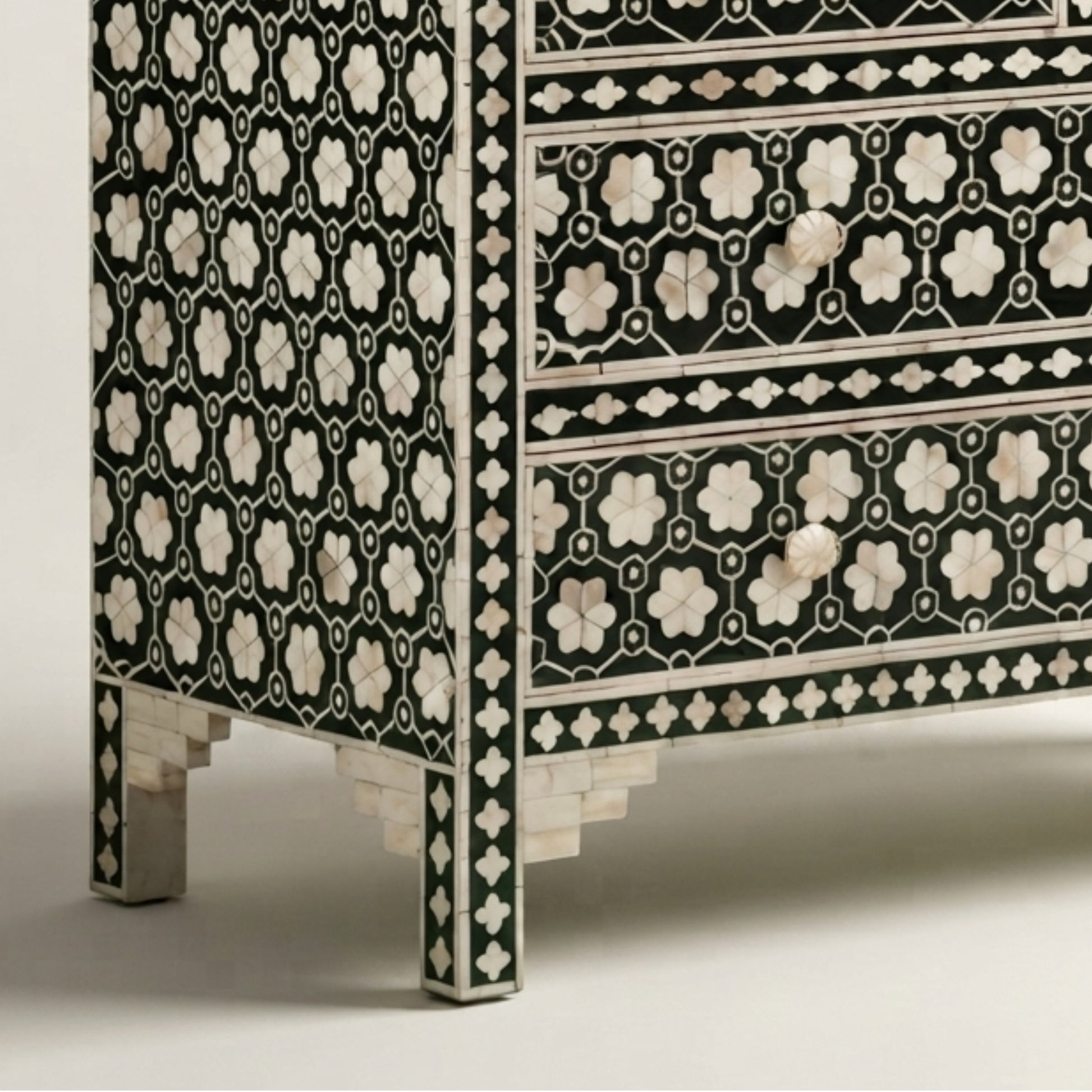 Close-up of a black and white mother-of-pearl inlaid chest of drawers, showing the detailed geometric floral patterns on the drawer fronts and side panel, with decorative legs.
