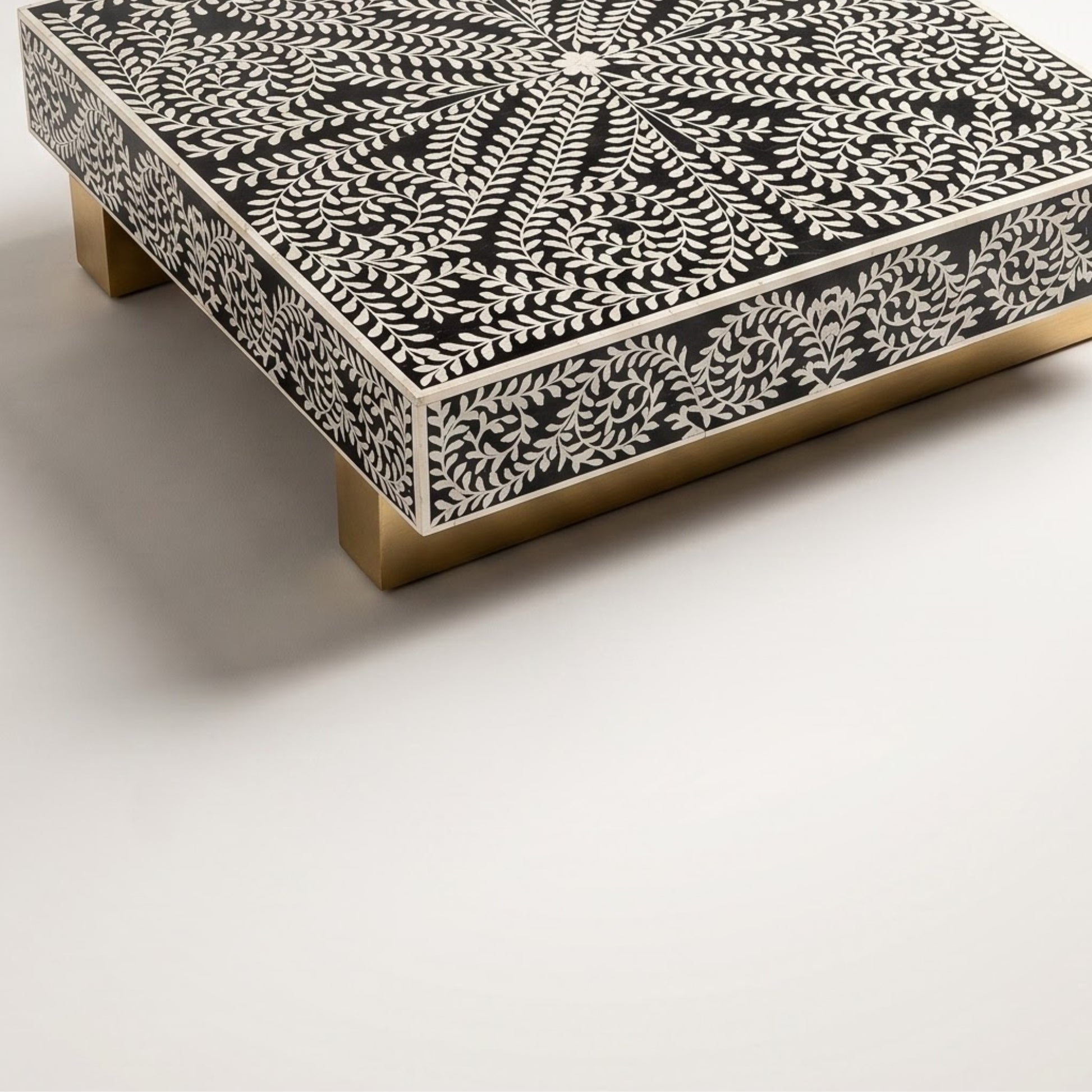 A square decorative table or stool with a black and white bone-inlay pattern and brass-colored legs, shown on a clean white background.