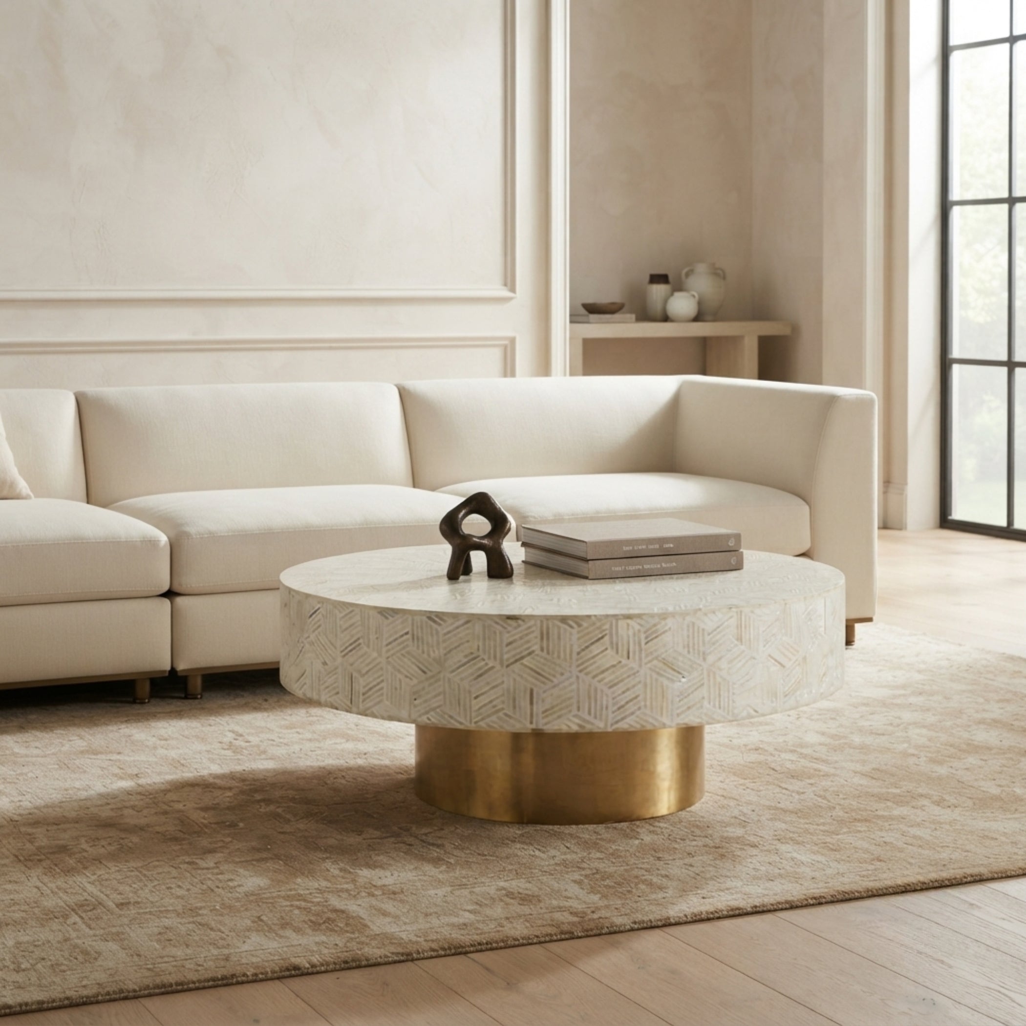 A round coffee table with a textured white stone top and a brushed gold metal base, styled in a modern living room next to a cream-colored sectional sofa.
