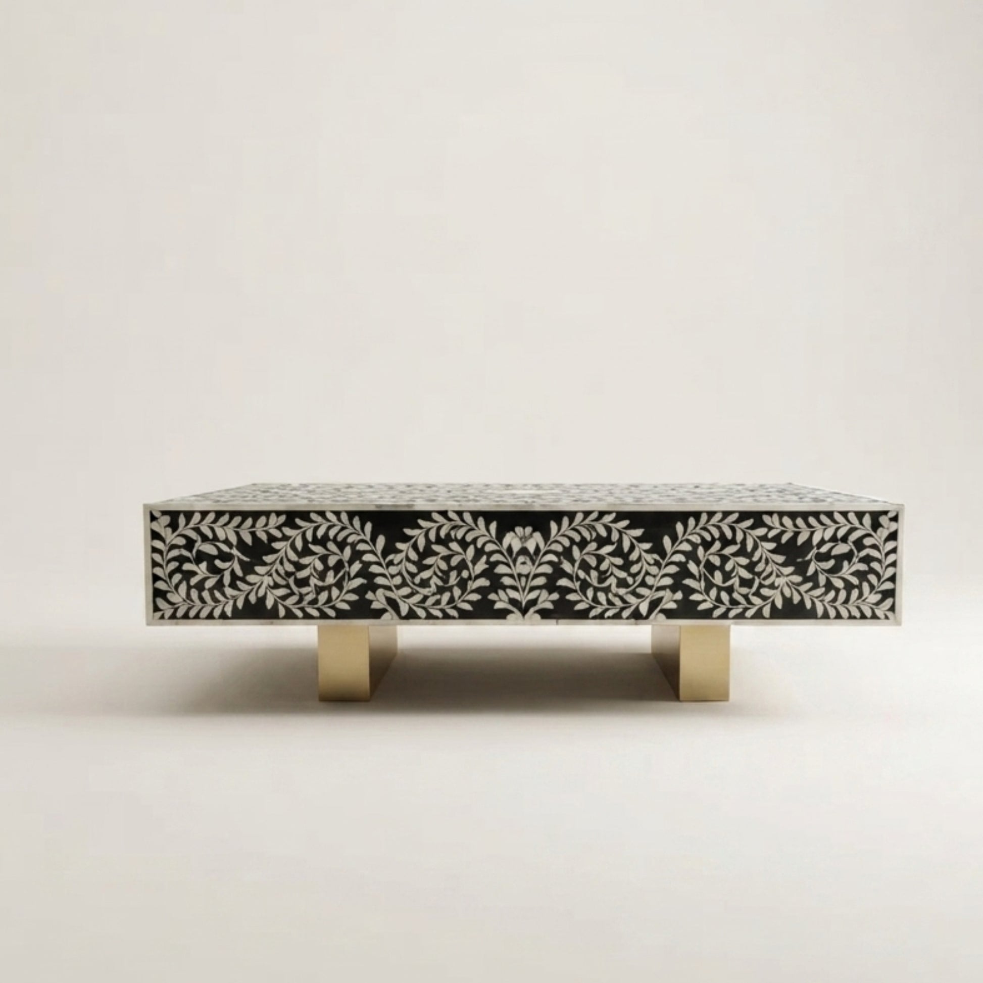 A rectangular coffee table with a black and white bone-in-shell patterned top and front, supported by two square gold metal legs, shown against a plain light gray background.
