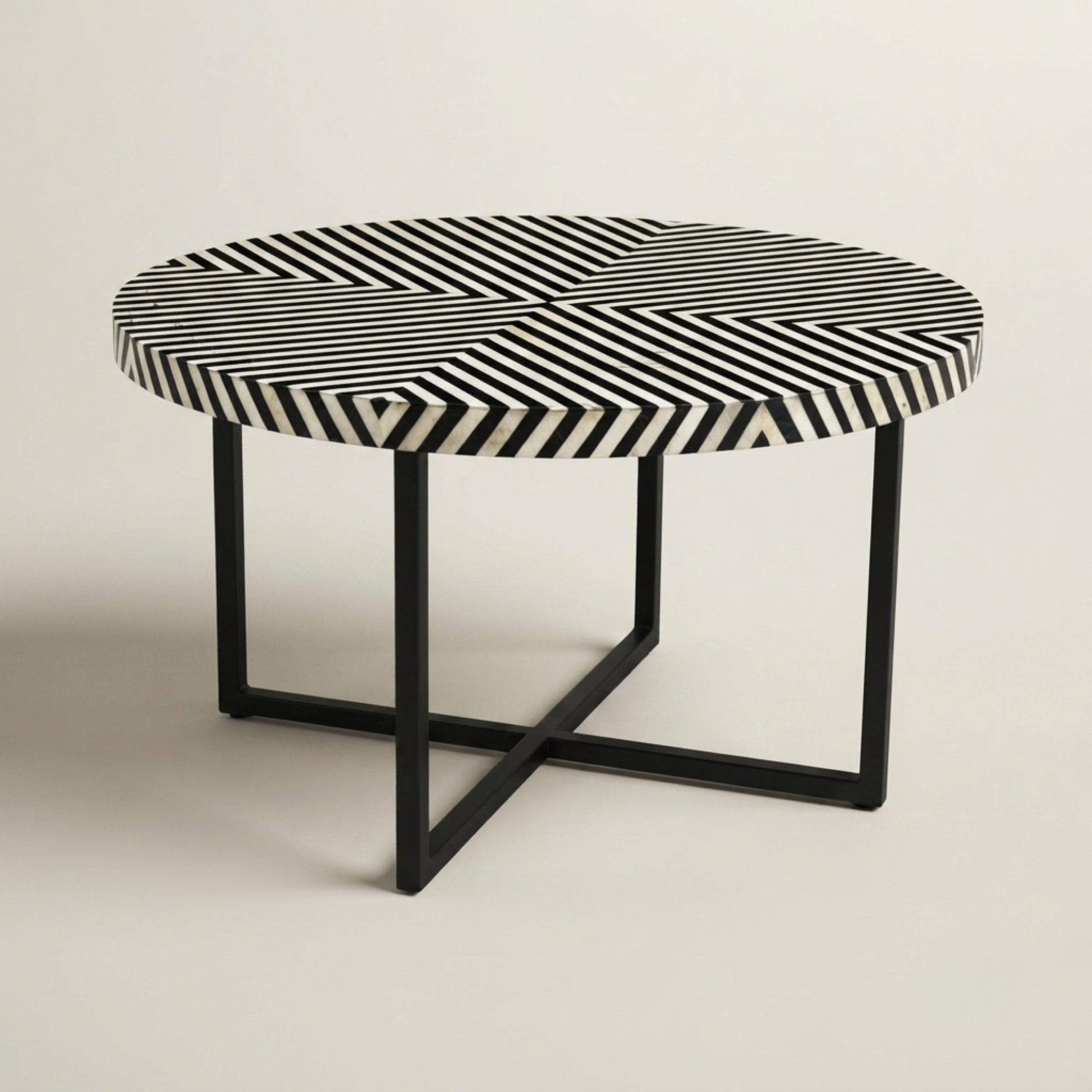A round accent table featuring a black and white striped bone-inlay top and a black metal frame base, set against a plain light beige background.