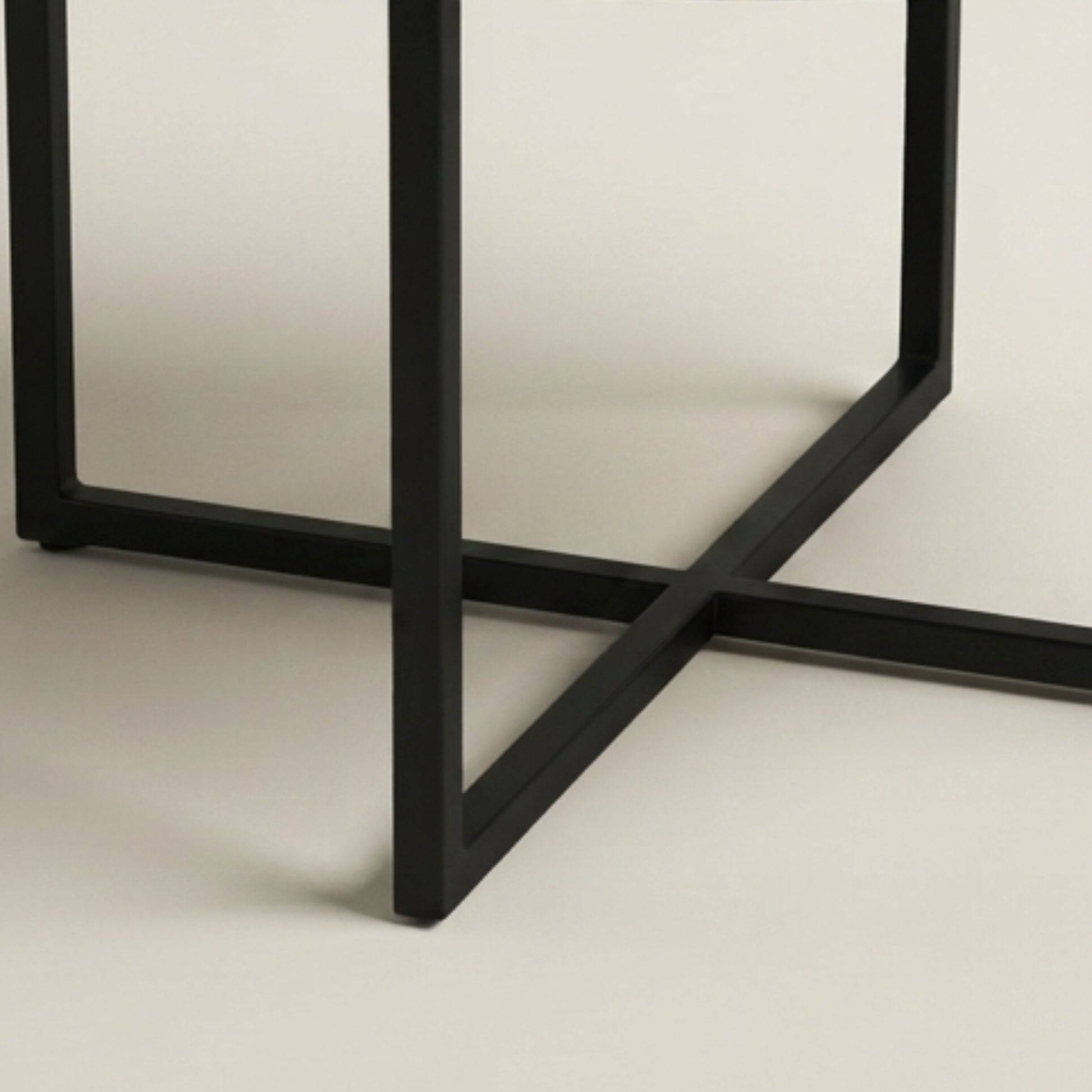 Close-up of a black metal table base with a geometric frame design on a light beige background.