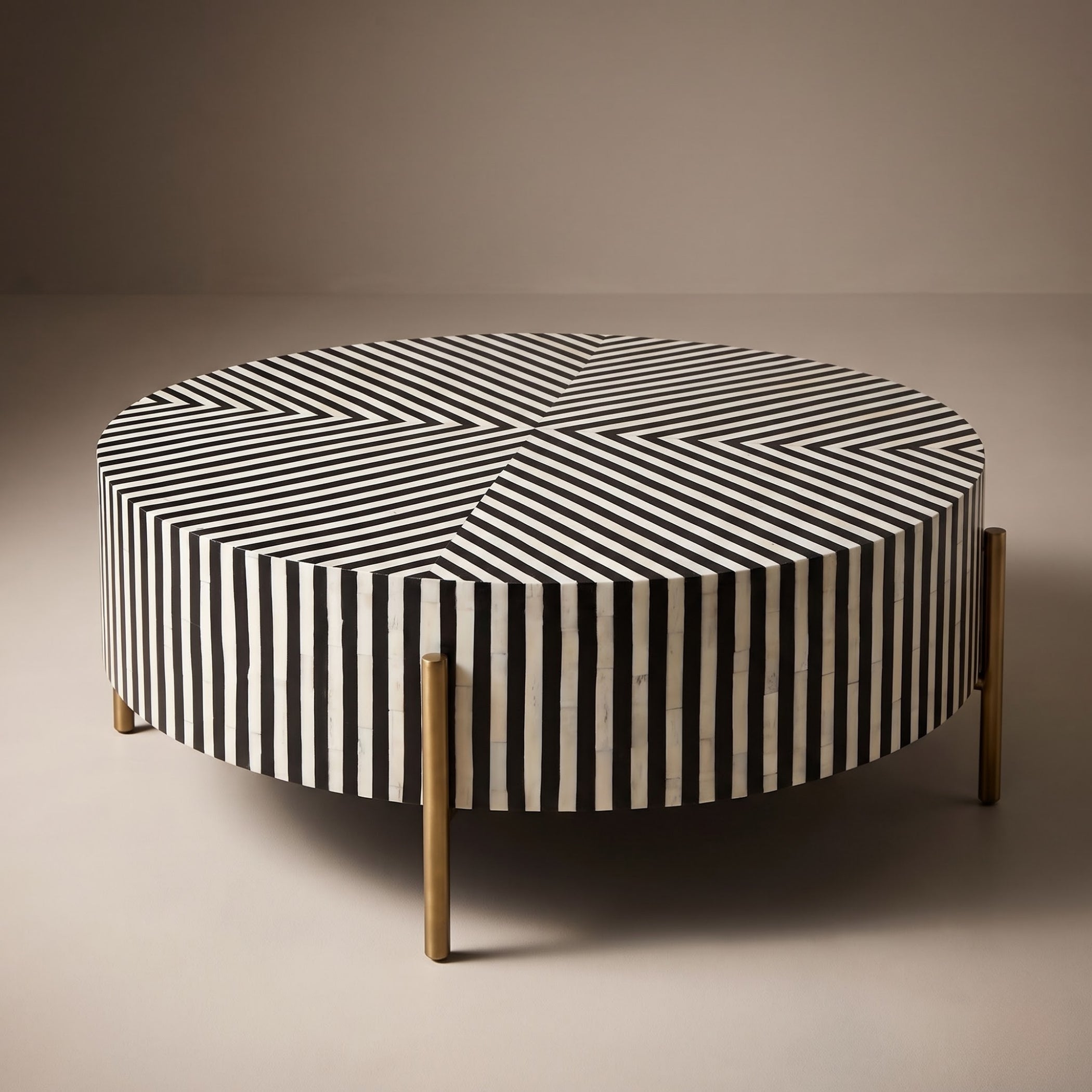 A round coffee table upholstered in black and white vertically striped bone-in-backer fabric, supported by four slim gold metal legs, set against a neutral beige background.