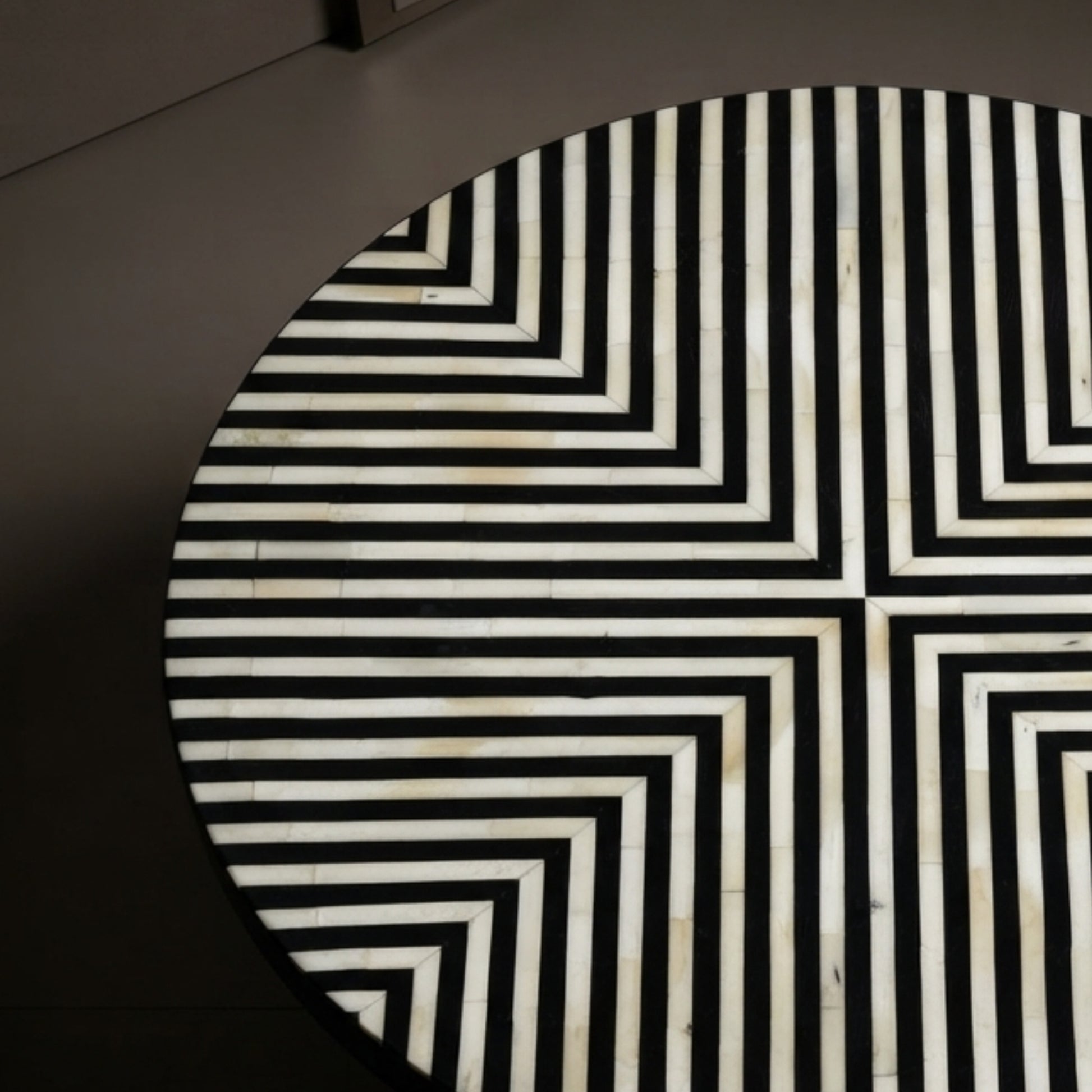 A close-up of a round table featuring a black and white geometric inlay pattern made of concentric rectangular lines.