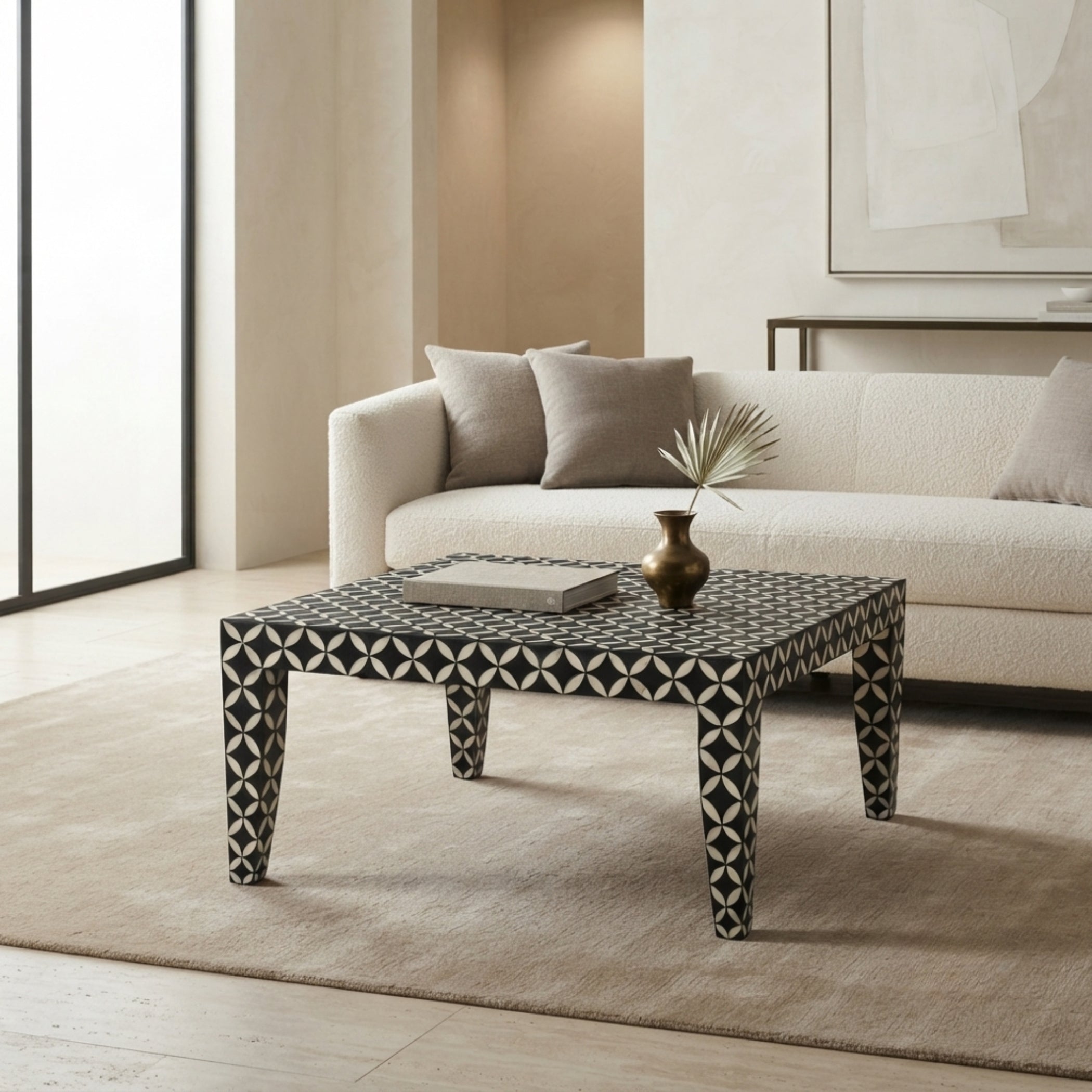 A square coffee table with a black and white geometric bone-inlay pattern, styled in a modern living room next to a cream bouclé sofa.