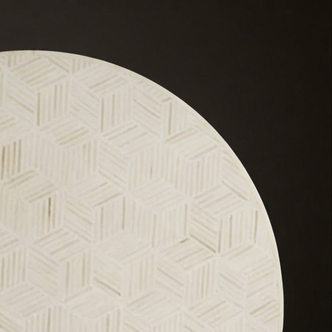 A round, off-white decorative plate or tray featuring an embossed geometric cube pattern, set against a dark gray background.