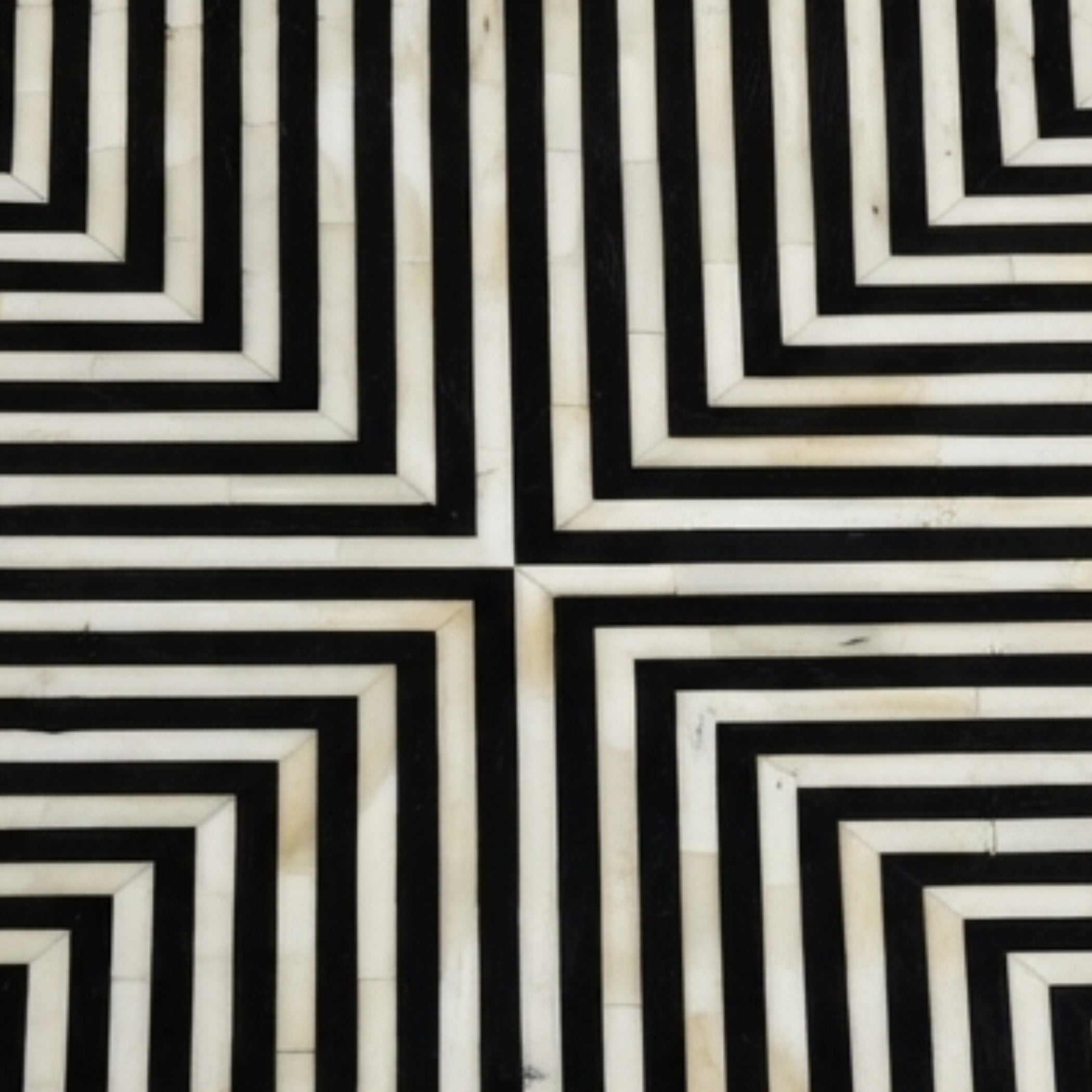 Black and off-white geometric patterned surface with repeating concentric angular stripes forming a maze-like design.