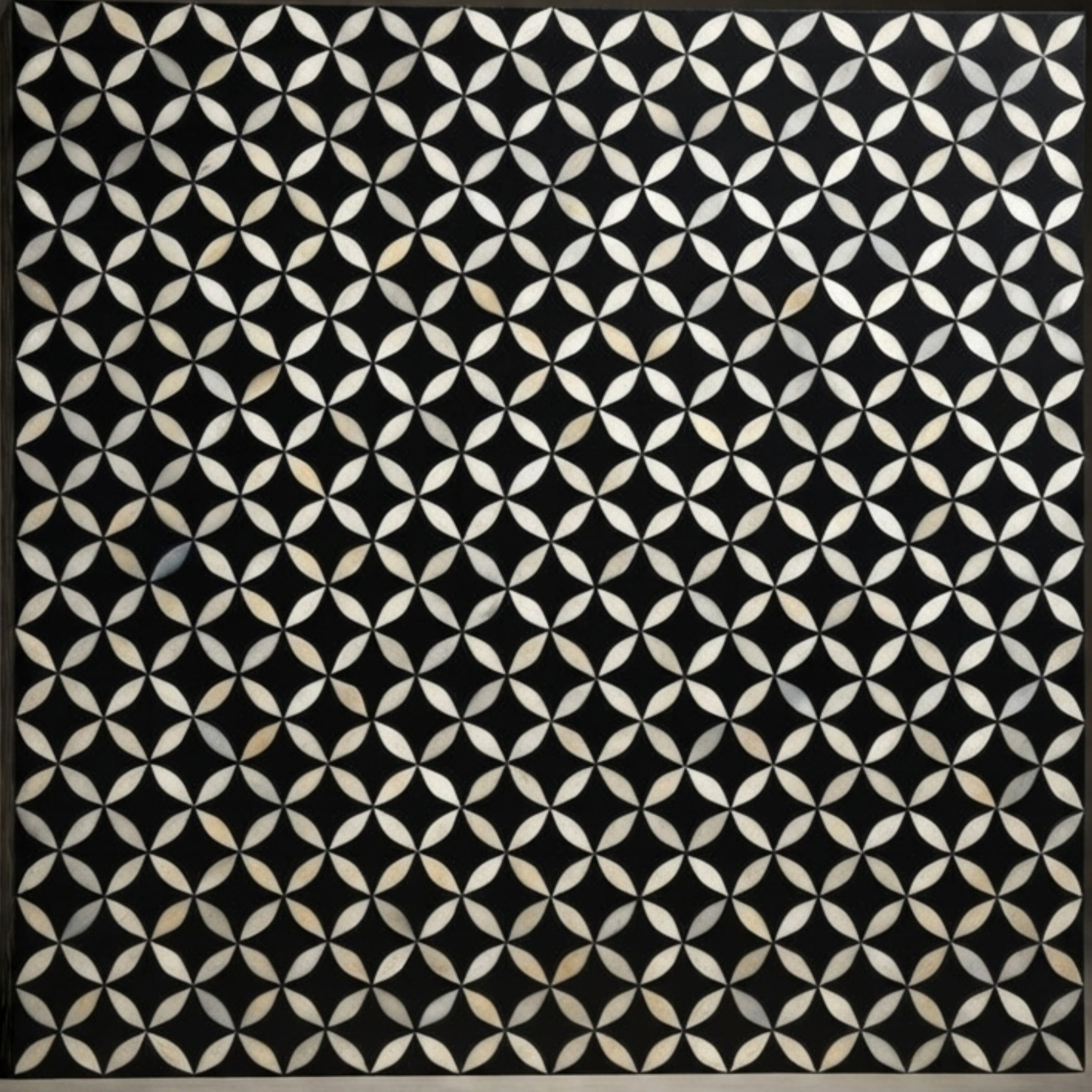 A square black panel featuring a repeating geometric pattern of interlocking white and beige petal-like shapes, bordered by a thin dark frame.