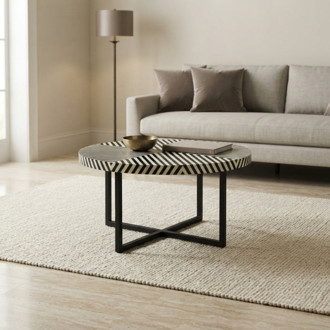 A round coffee table with a black and white chevron-patterned top and black metal legs, styled in a modern living room setting on a textured rug in front of a light gray sofa.