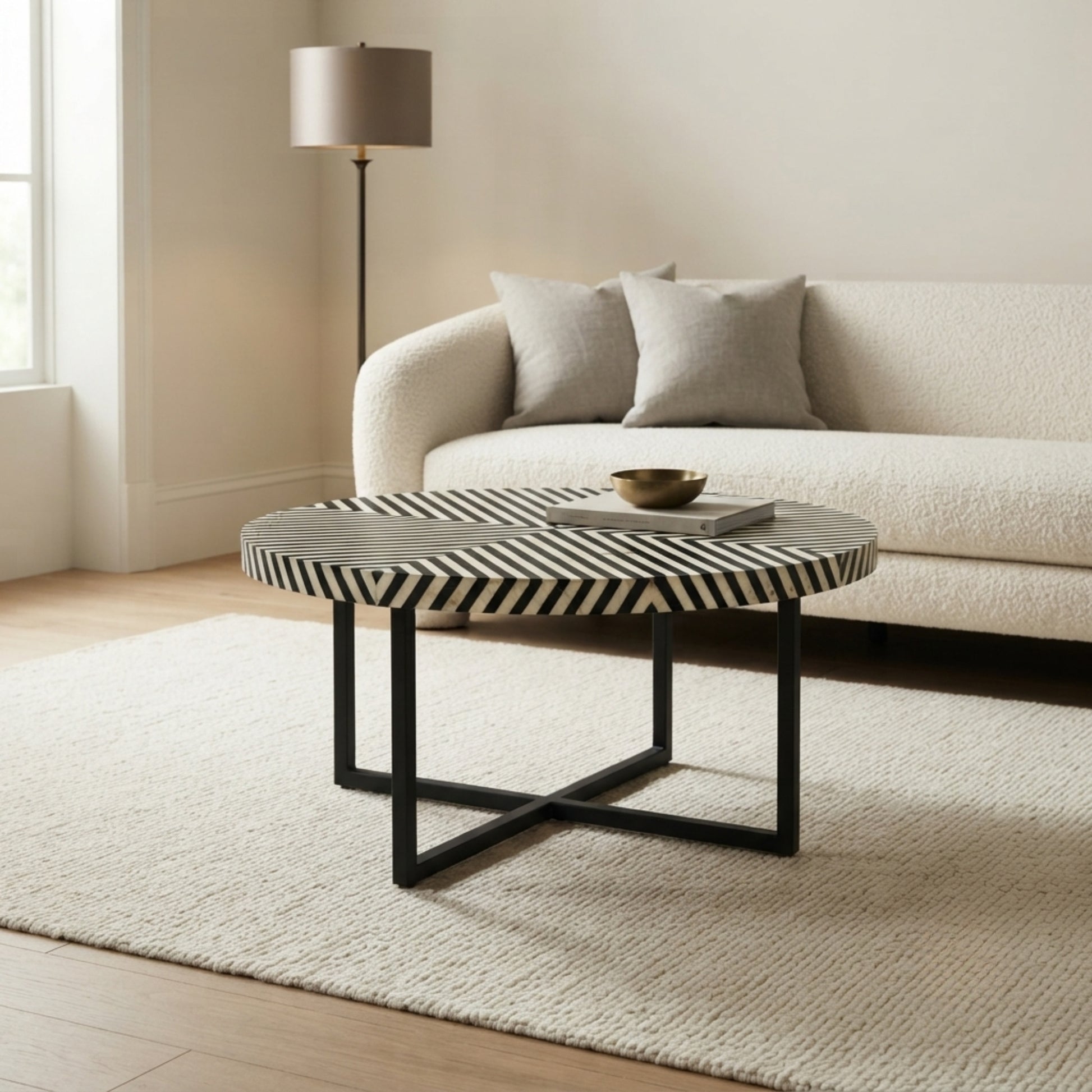 A round coffee table with a black and white chevron-patterned top and black metal legs, styled in a modern living room setting in front of a cream boucle sofa.