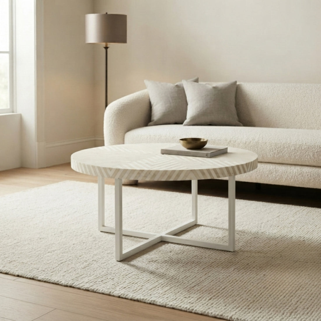 A round white coffee table with a textured chevron-patterned top and white metal legs, styled in a bright, modern living room next to a cream boucle sofa.