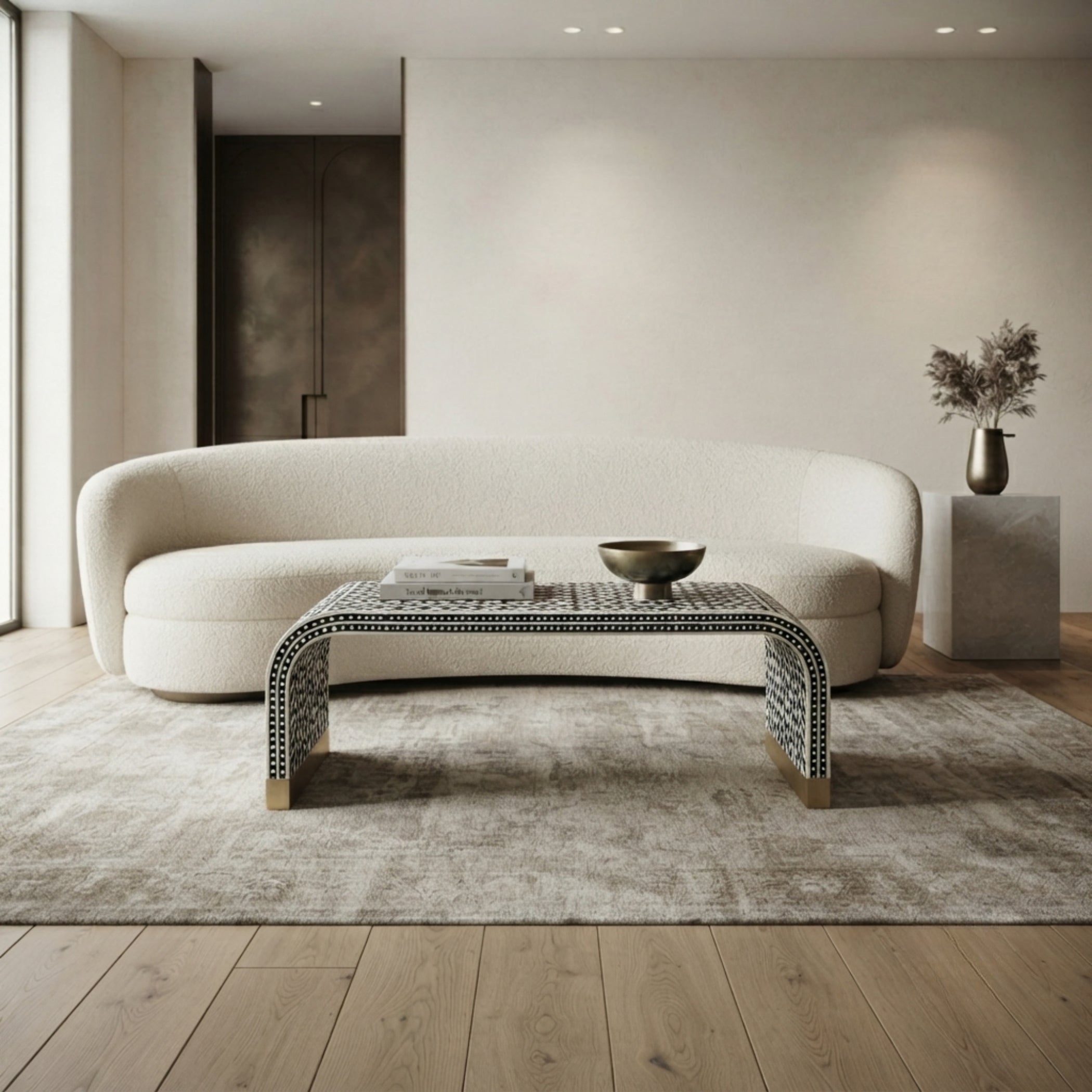 A modern curved cream bouclé sofa in a minimalist living room, styled with a low black-and-white patterned coffee table on a light gray rug over light wood flooring.