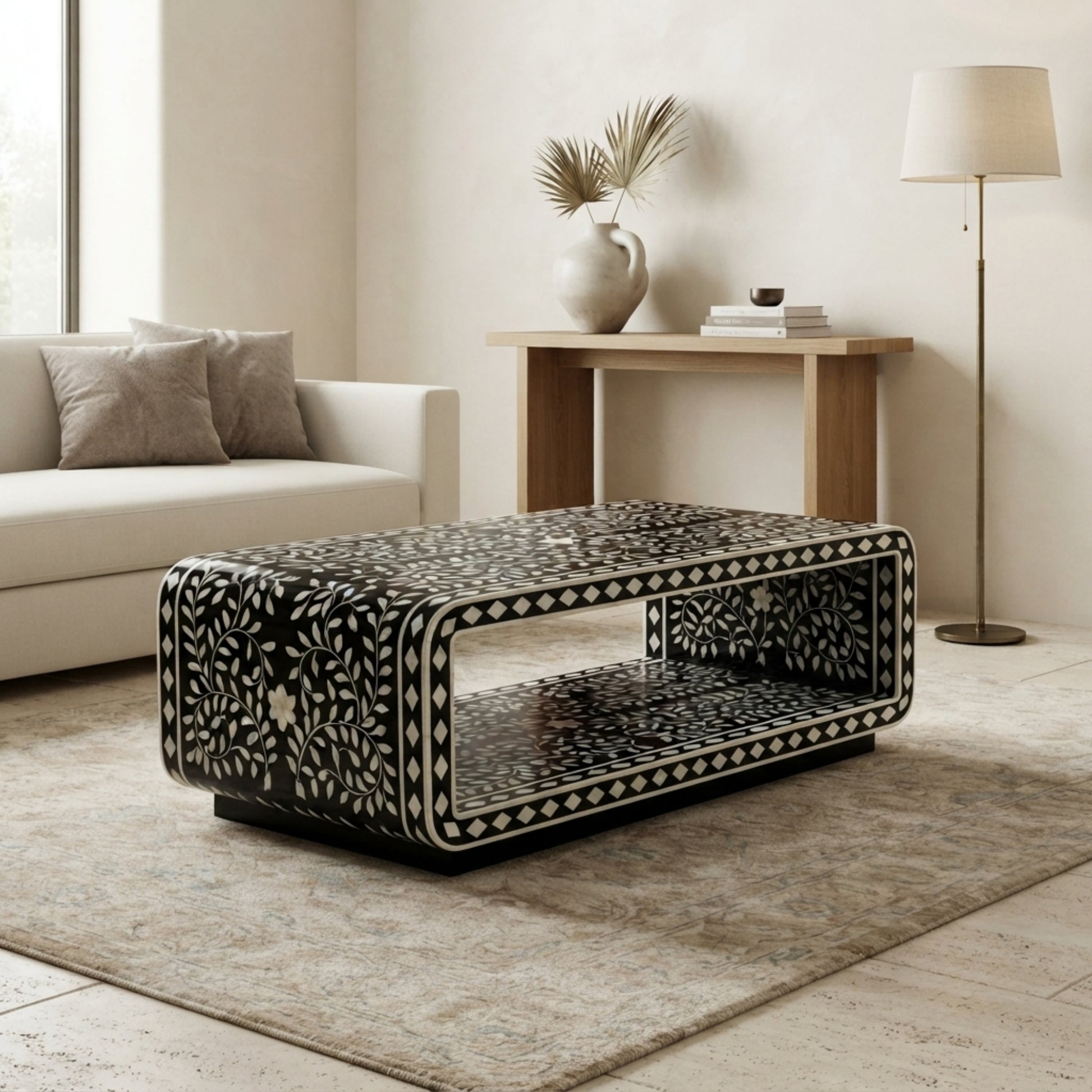 A rectangular black coffee table with an intricate white bone-inlay floral pattern, styled in a modern living room setting on a beige rug.
