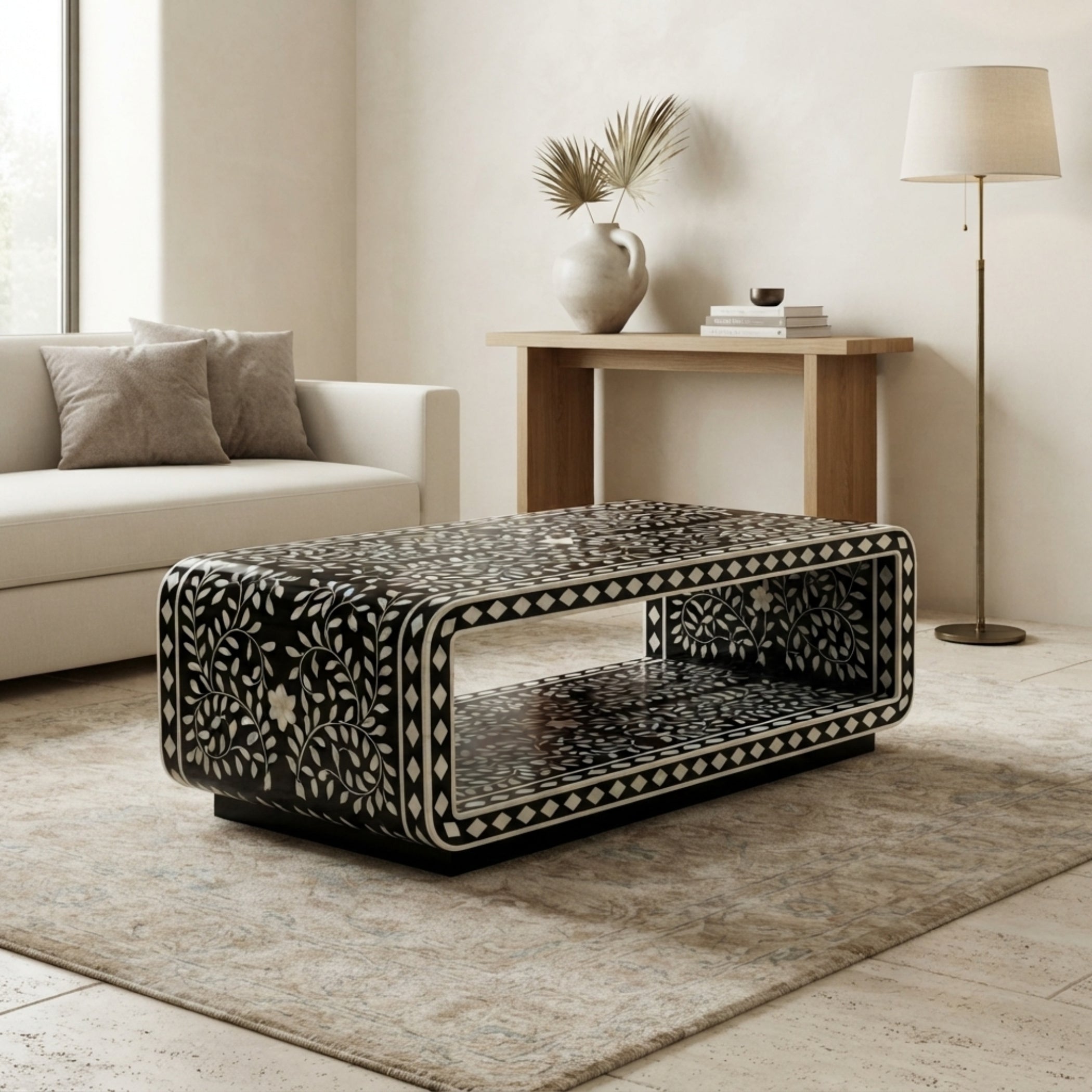 A rectangular black coffee table with an intricate white bone-inlay floral pattern, styled in a modern living room setting on a beige rug.