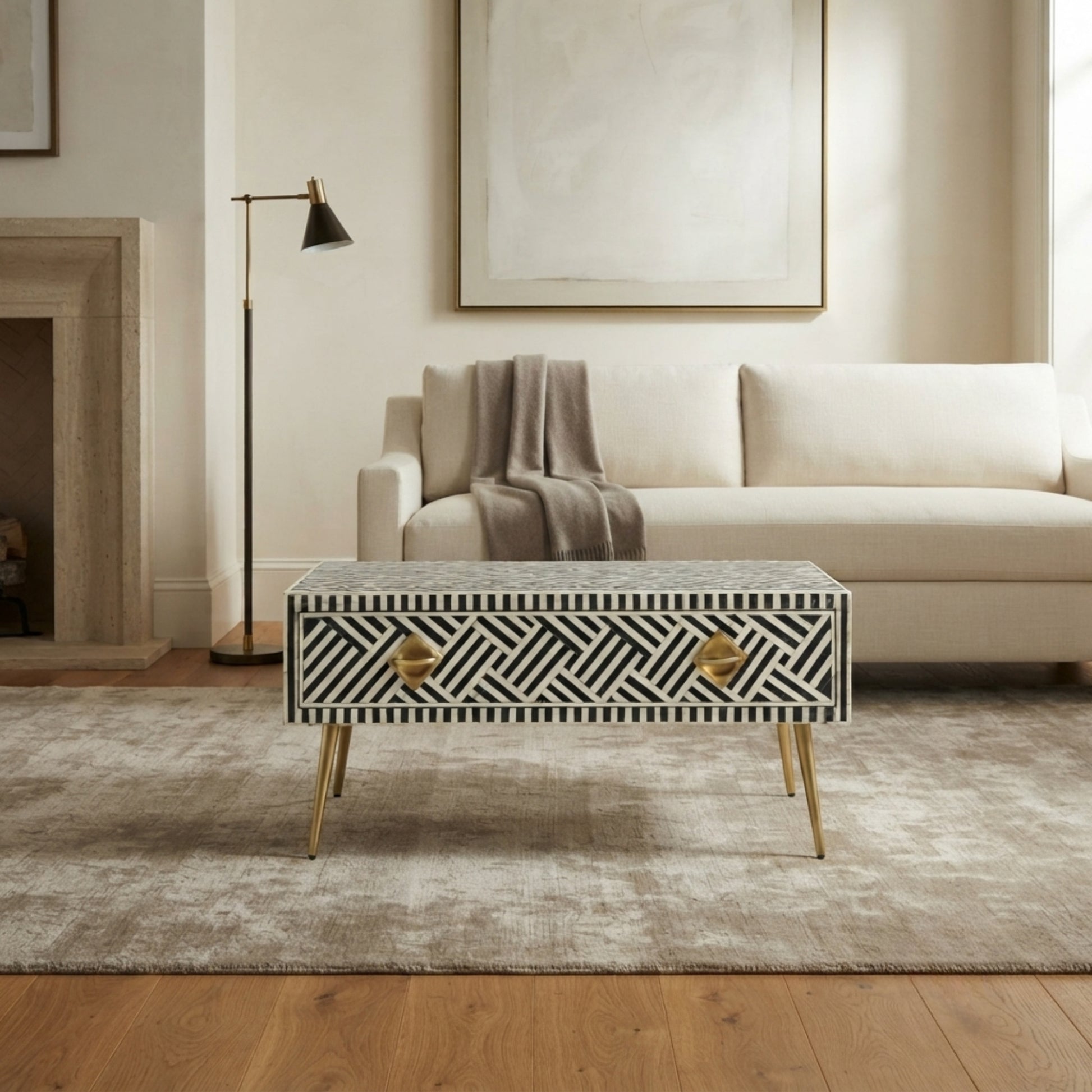 A rectangular coffee table with a black and white geometric bone-inlay pattern and gold legs, styled in a modern living room setting.